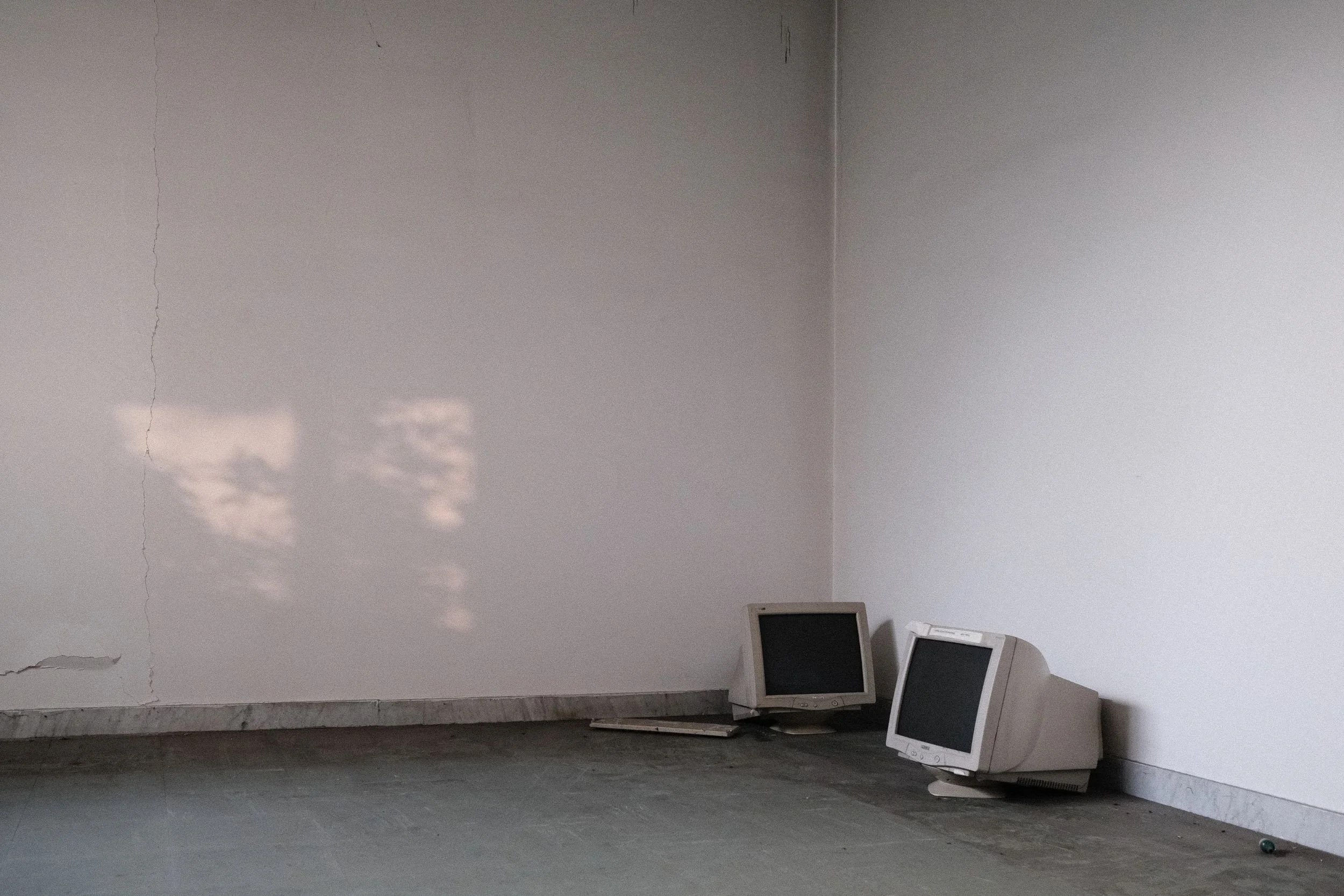 Two old computer monitors sitting in the corner of a classroom in an abandoned school