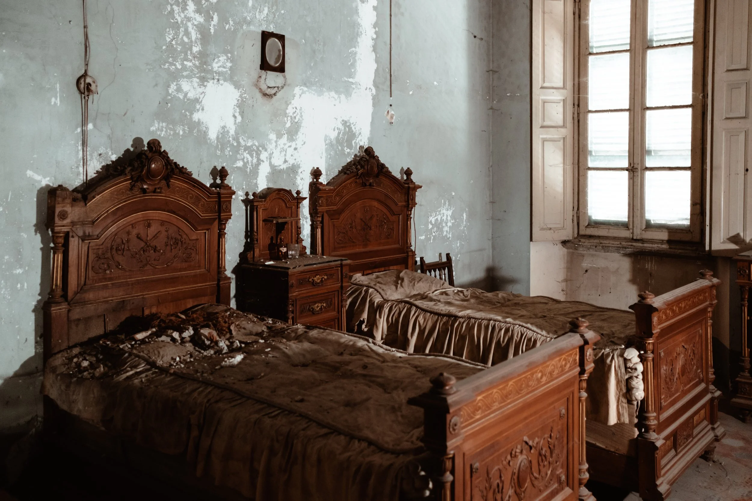 Two carved wooden beds in a bedroom where the plaster is falling away