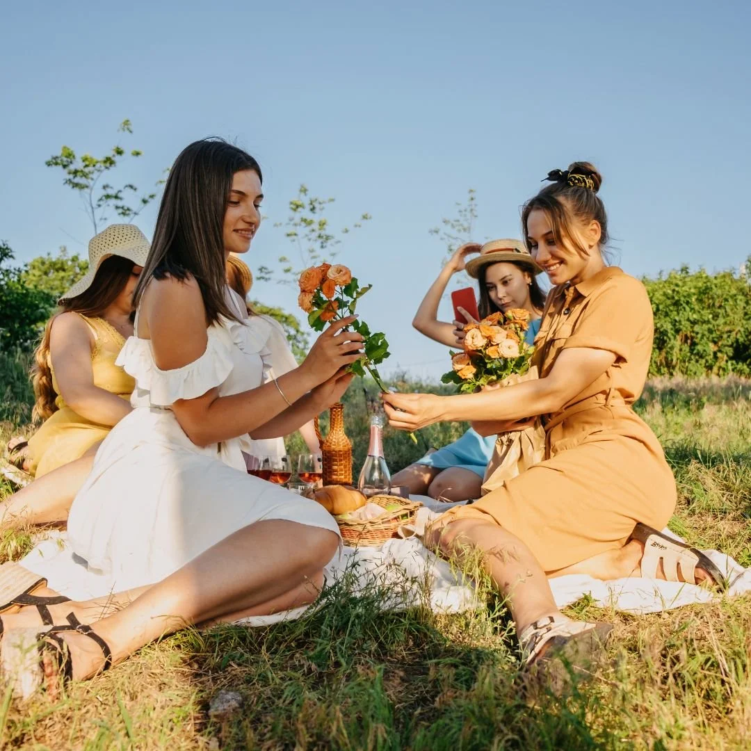 Four women friends having a picnic outside with flowers all around