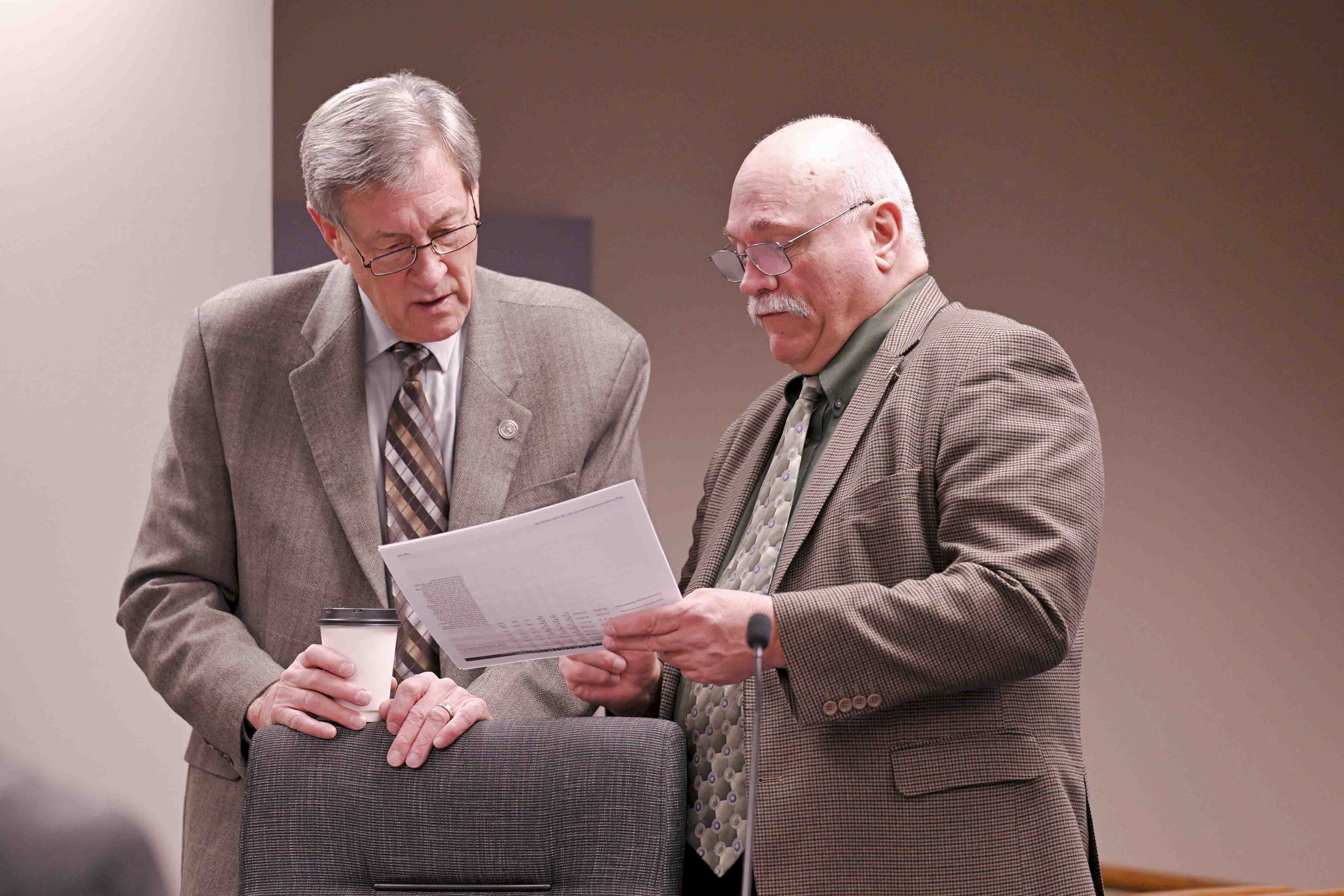Two older men in business suits discussing a document in a conference room.