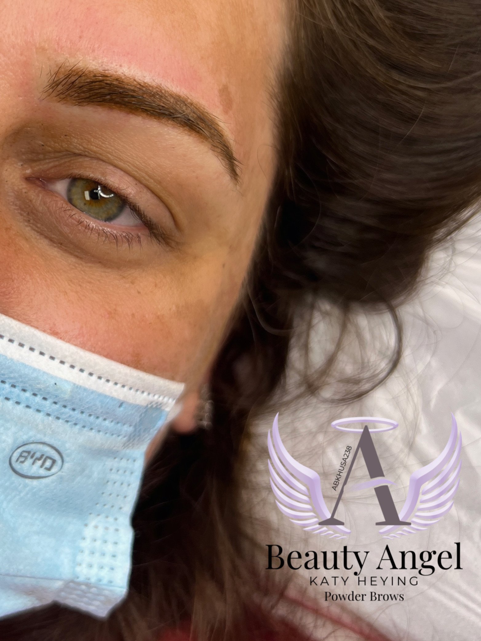 A close-up of a woman lying down, wearing a light blue face mask, with well-groomed eyebrows and brown hair. The image features a logo for 'Beauty Angel' by Katy Heying, focusing on powder brows.