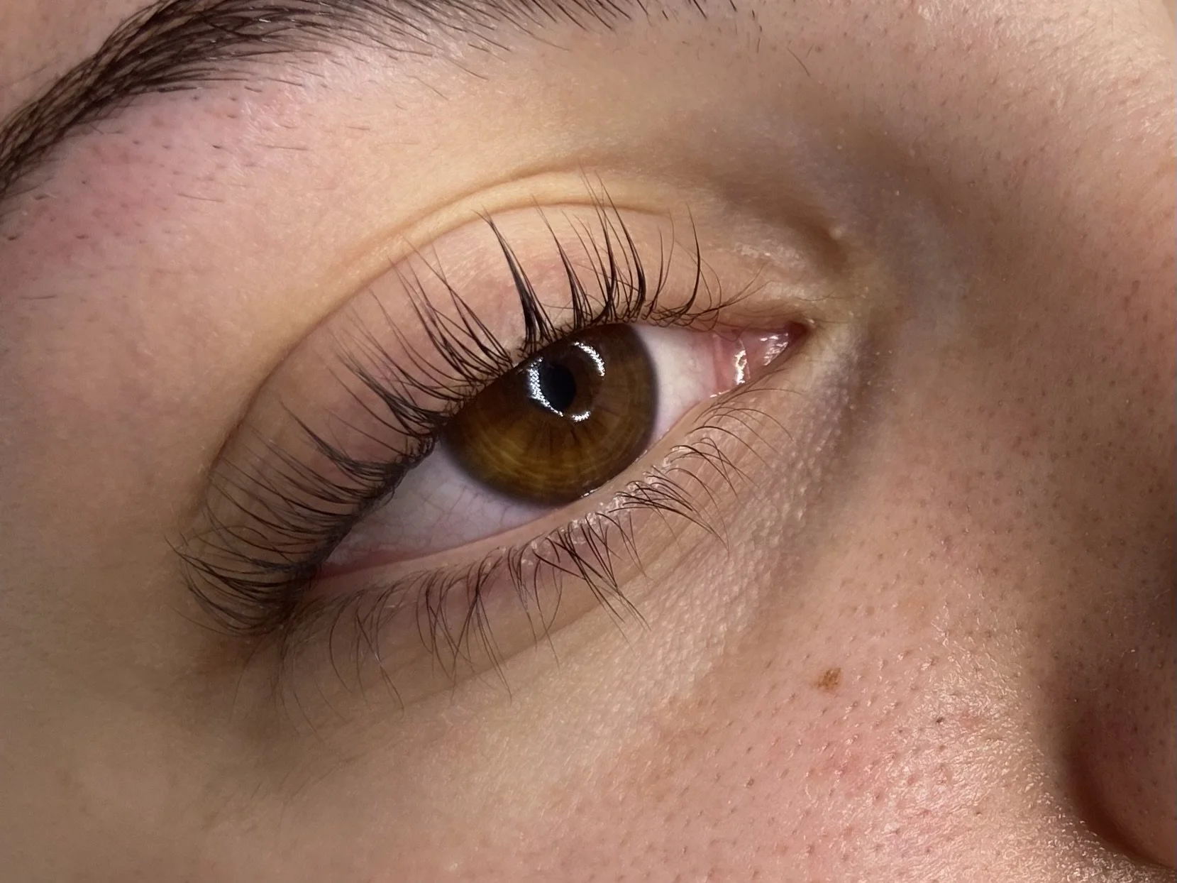 Close-up of a person's eye showing brown iris, long eyelashes, and detailed skin texture near the eye.