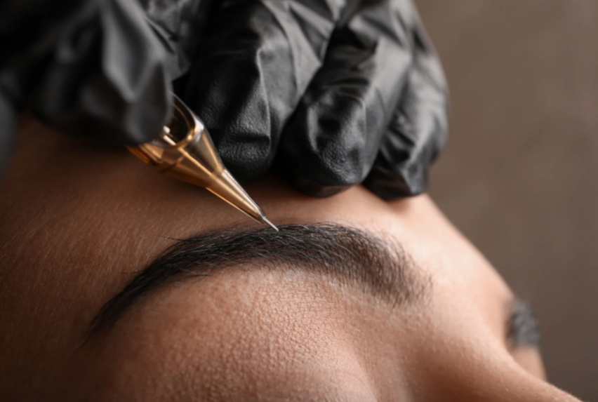 Close-up of a person receiving an eyebrow tattooing or microblading procedure with a technician holding a fine needle tool.