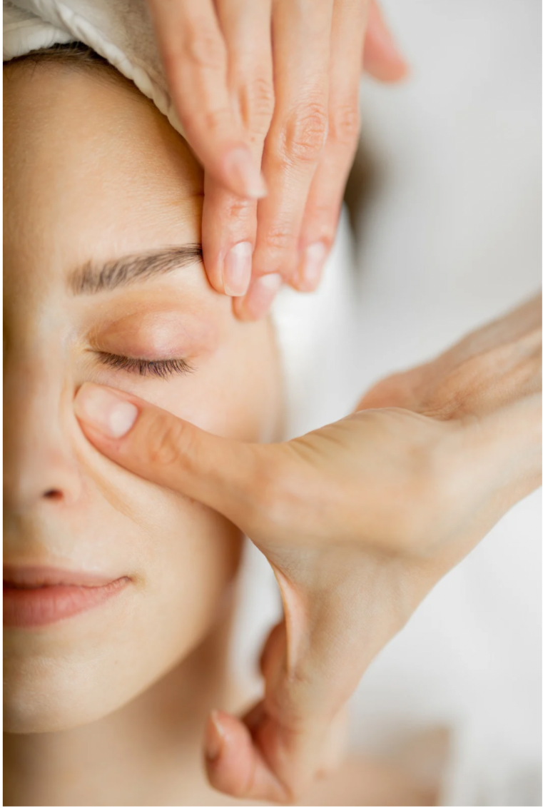 Person receiving a facial massage with a hand applying pressure on the forehead and another on the cheek, eyes closed.