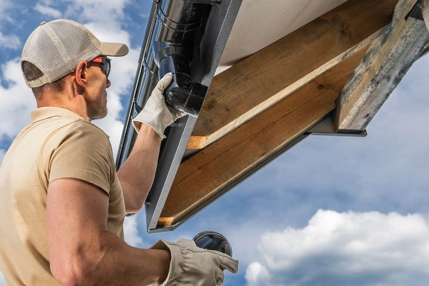 Professional gutter installer securing a black downspout to the roof edge of a residential home
