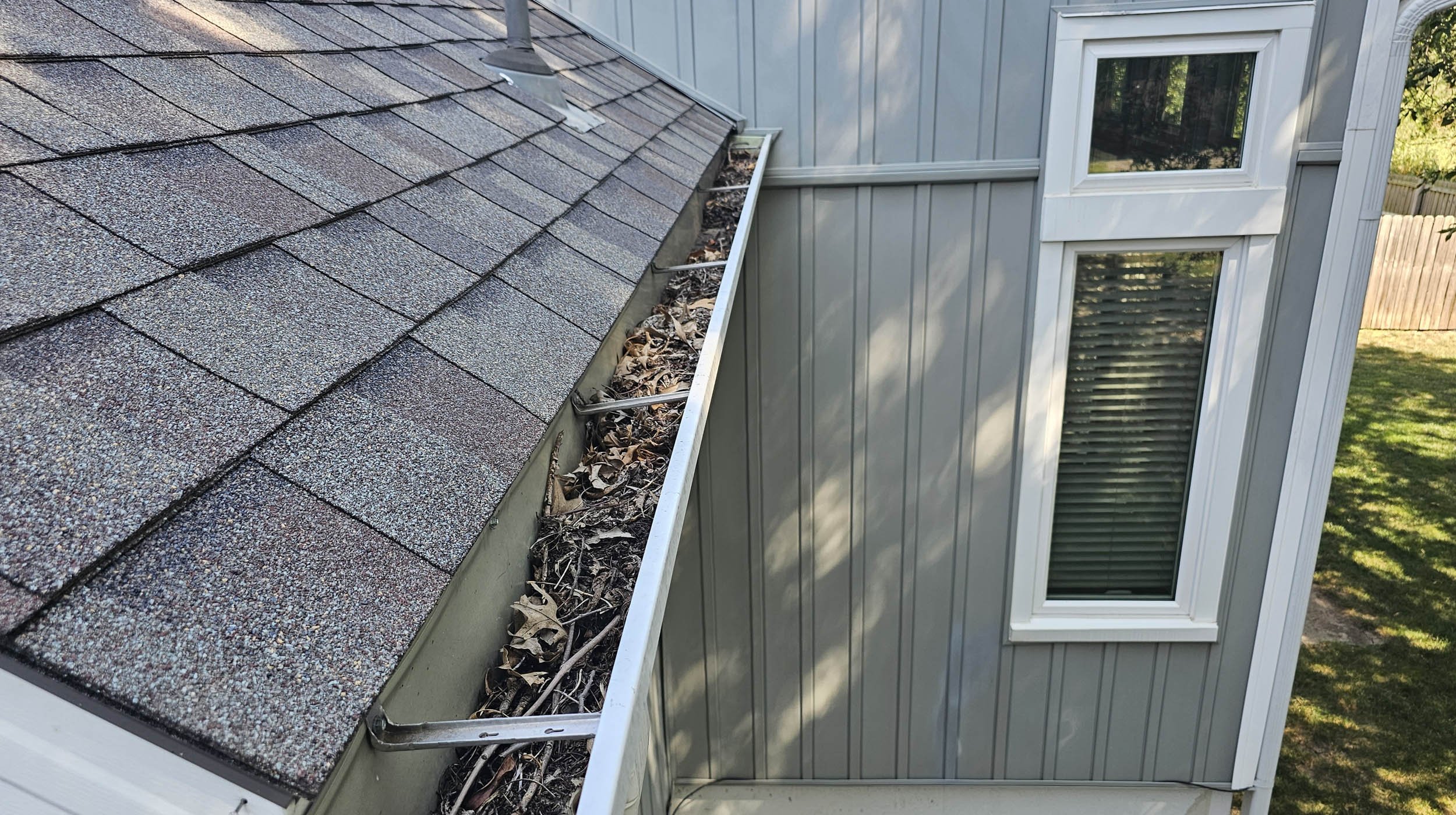 Clogged house gutters filled with leaves and debris along a shingled roof