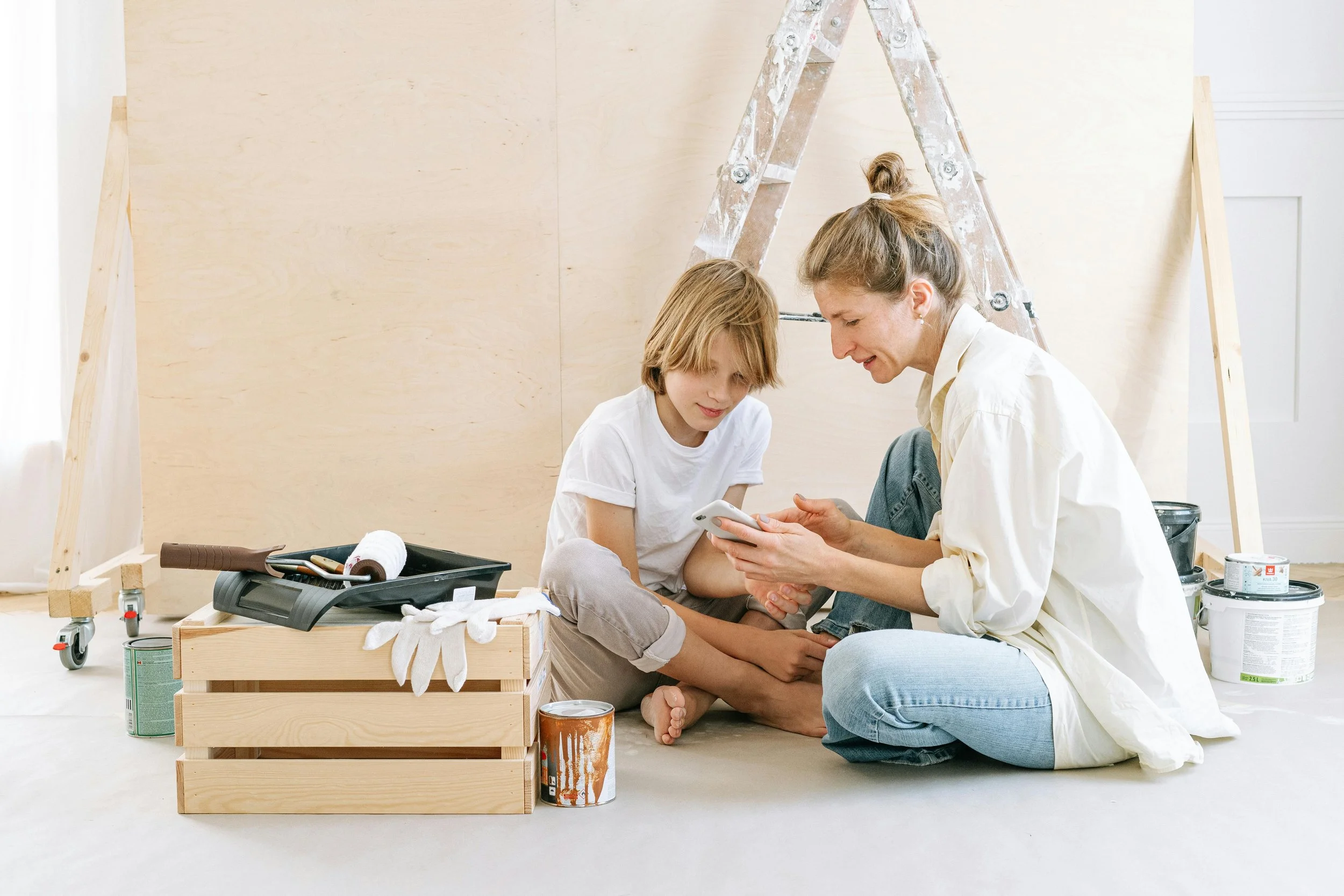 Mother and son working on a room renovation project, seated on the floor with painting supplies.