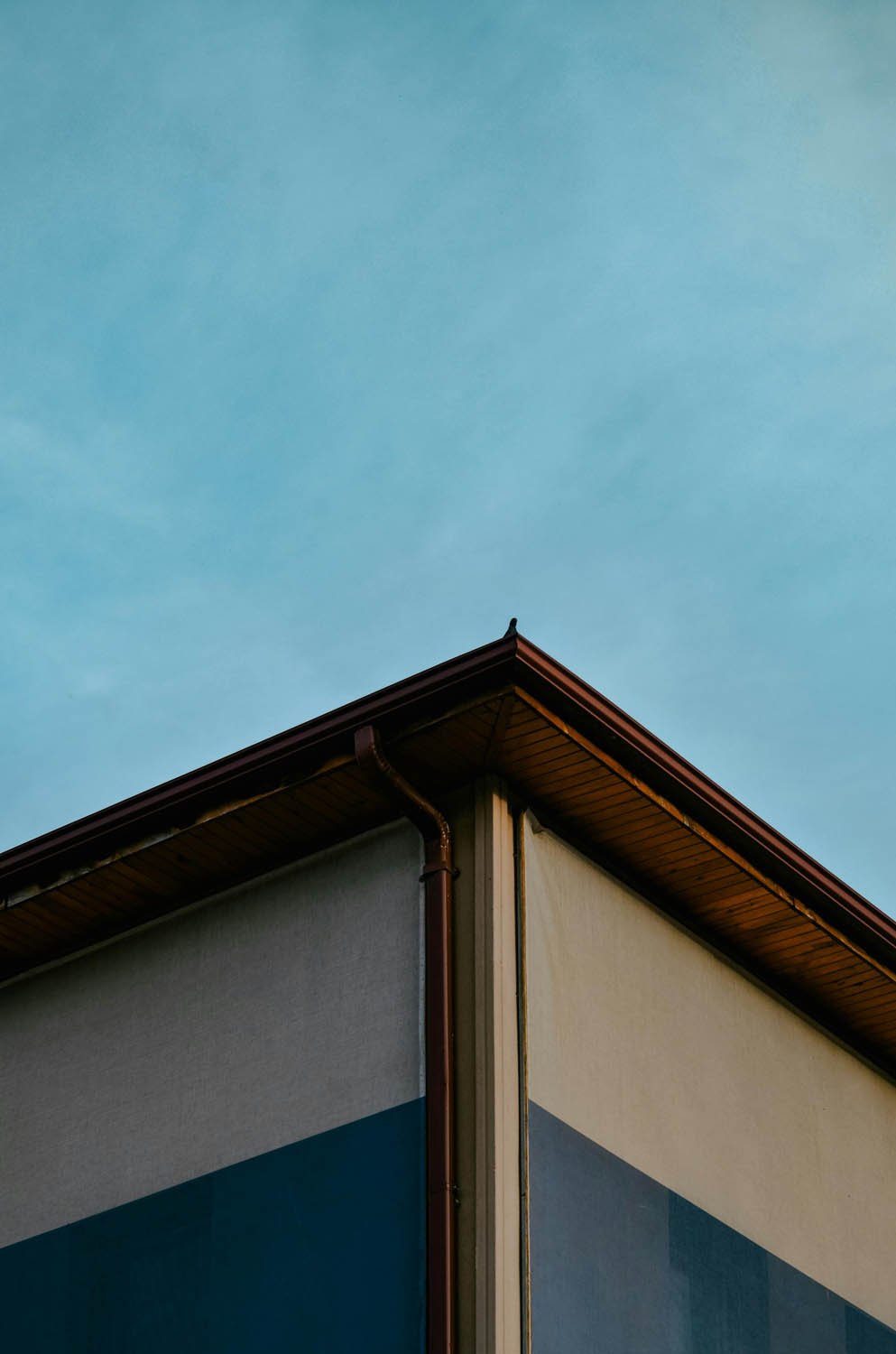 Exterior corner detail of a house with newly installed seamless brown gutters and matching downspout