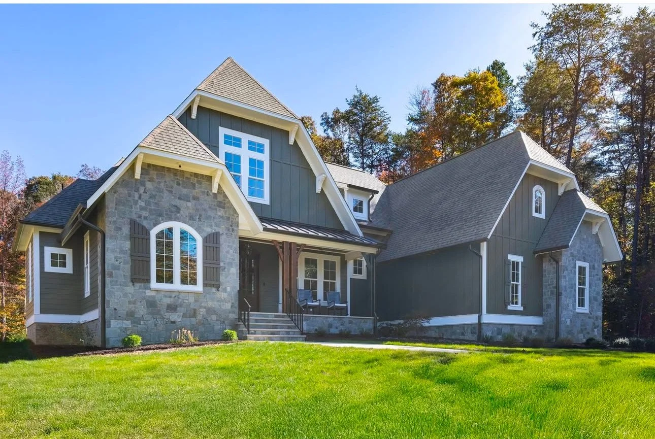 Custom Craftsman-style home with gray board-and-batten siding, stone façade, white trim, and professionally installed white gutters