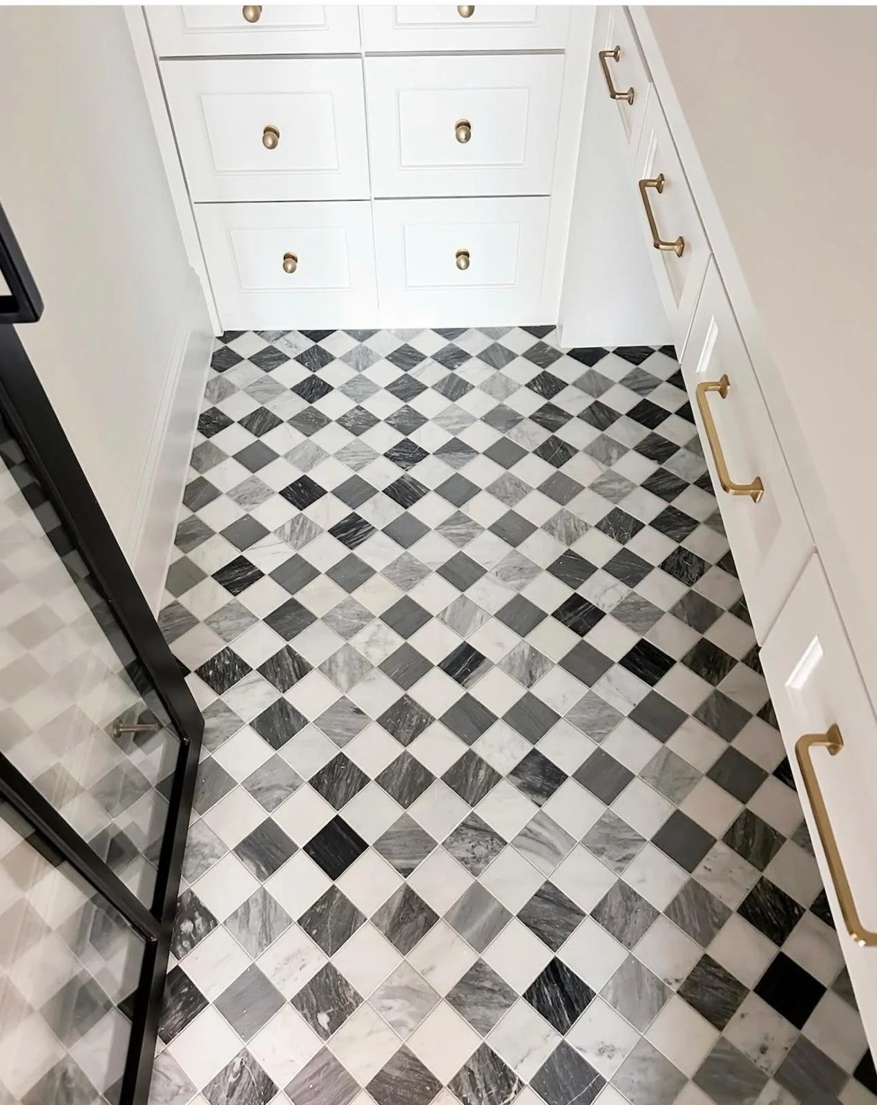 Black, white, and gray diamond pattern tiled floor in a kitchen corner with white cabinets and gold handles.