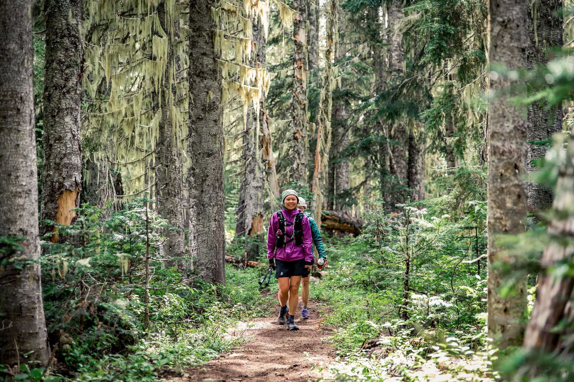  Two female runners on a forest trail with moss in the sunlight 