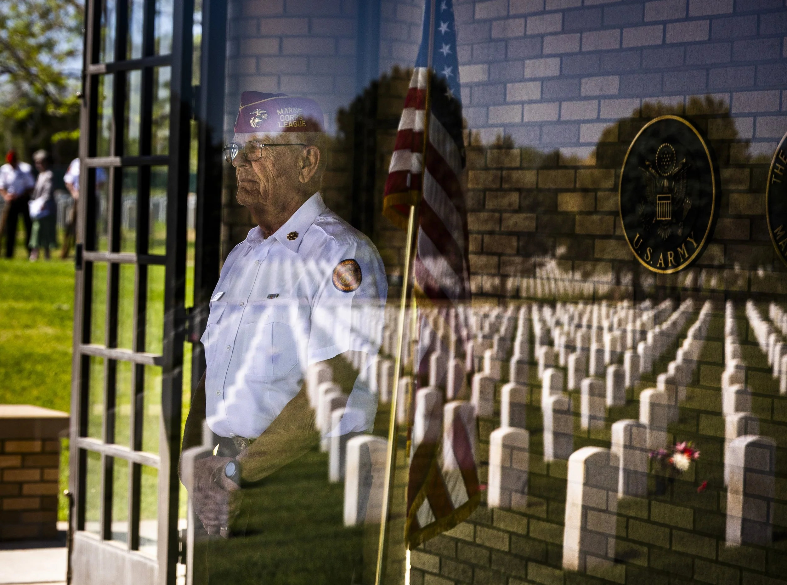 Rows of graves are reflected through a window onto Union Colony Marines Detachment 1093 Honor Guard member Clem Schuette as he solemnly waits for the arrival of a burial party for a passed veteran whose burial service he will officiate, at Fort Logan