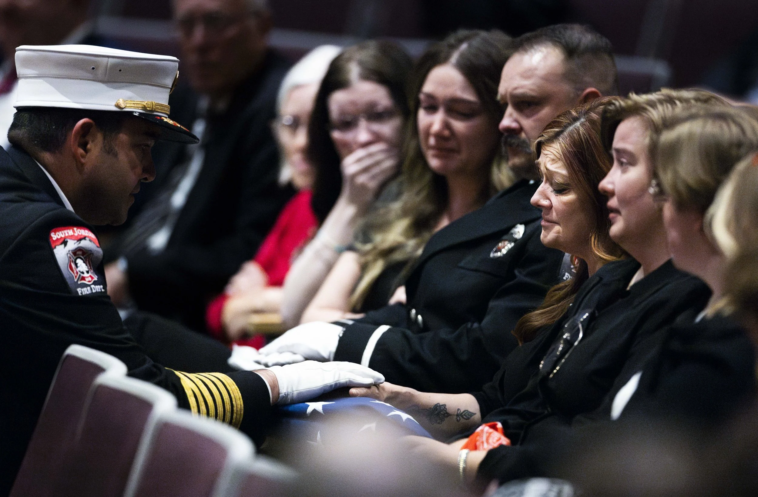 A firefighter presents the flag from the casket to the wife of the late South Jordan firefighter Corban Summers, Kim Summers, during a funeral service for Summers at Hunter High School in West Valley on Saturday, April 26, 2025.