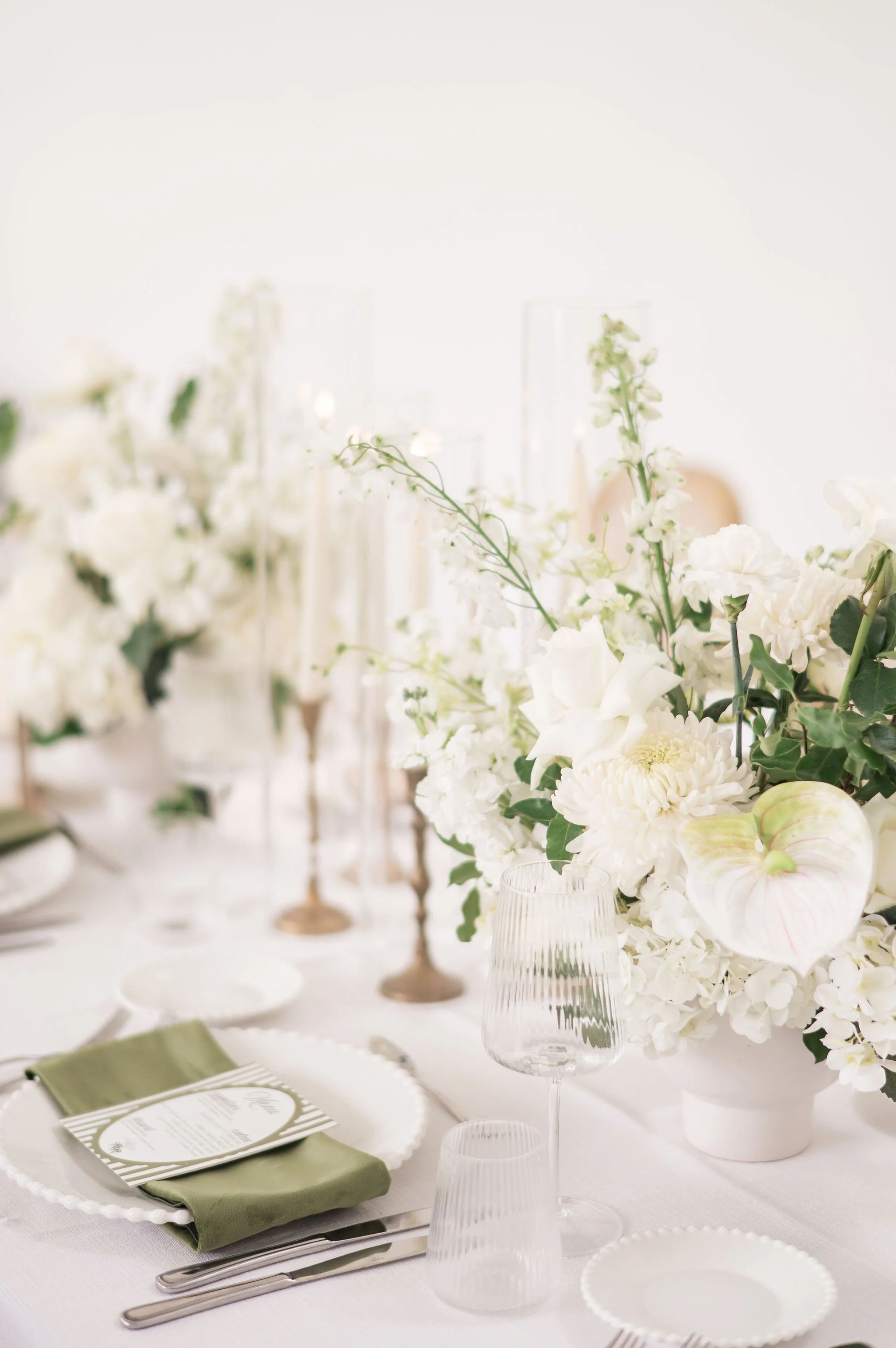 Elegant table setting with white floral centerpiece, green napkins, and clear glassware on a white tablecloth for a formal event.