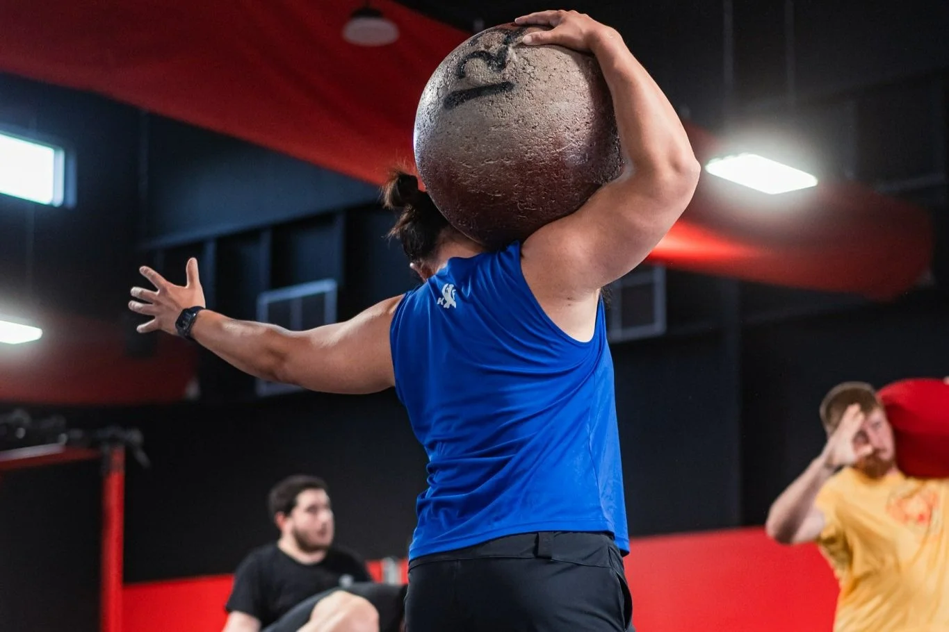 Person lifting a heavy stone in a gym environment, wearing a blue sleeveless shirt.
