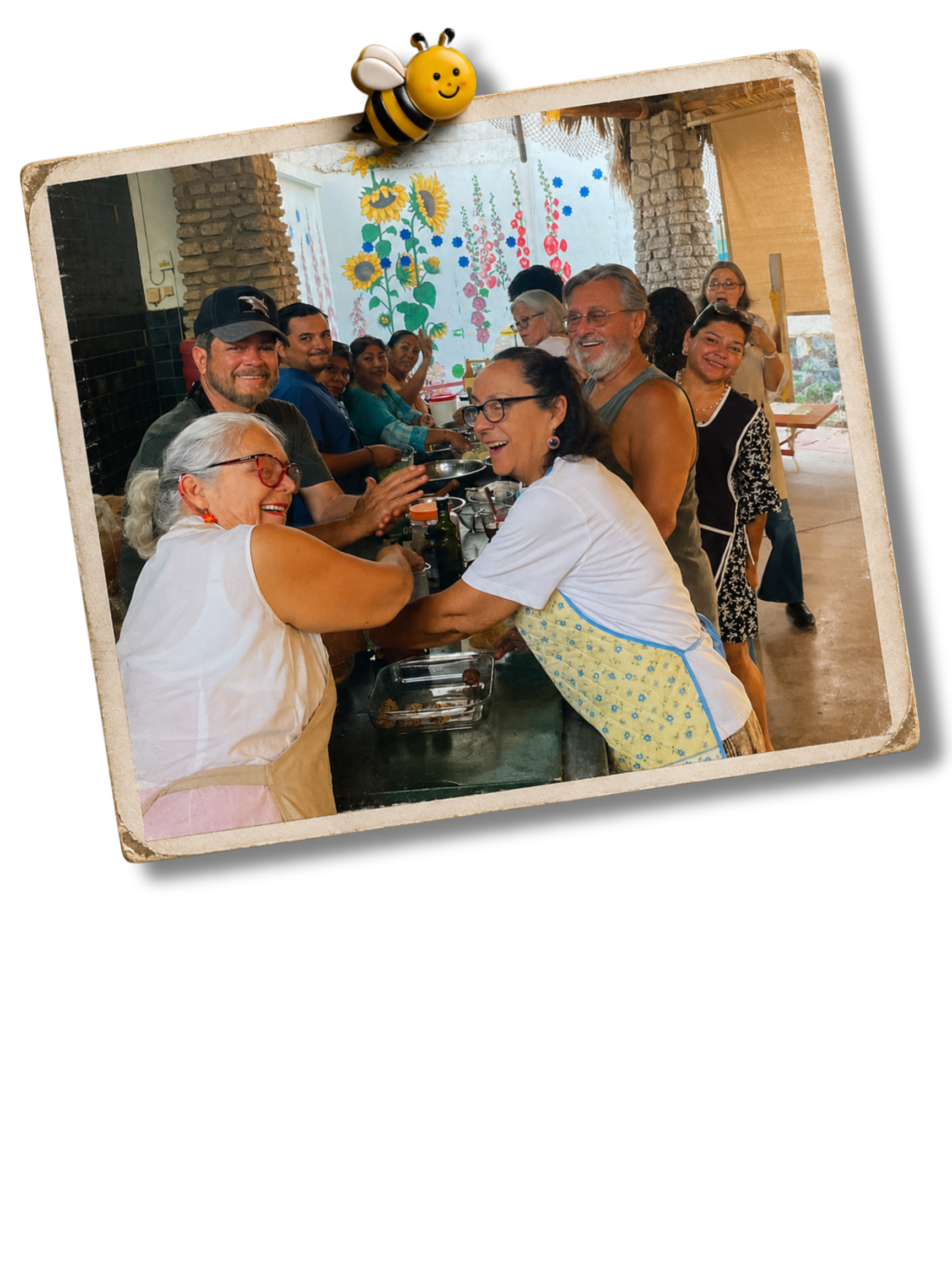 Grupo de personas en una celebración, sonriendo y conversando en un ambiente decorado con flores en la pared.
