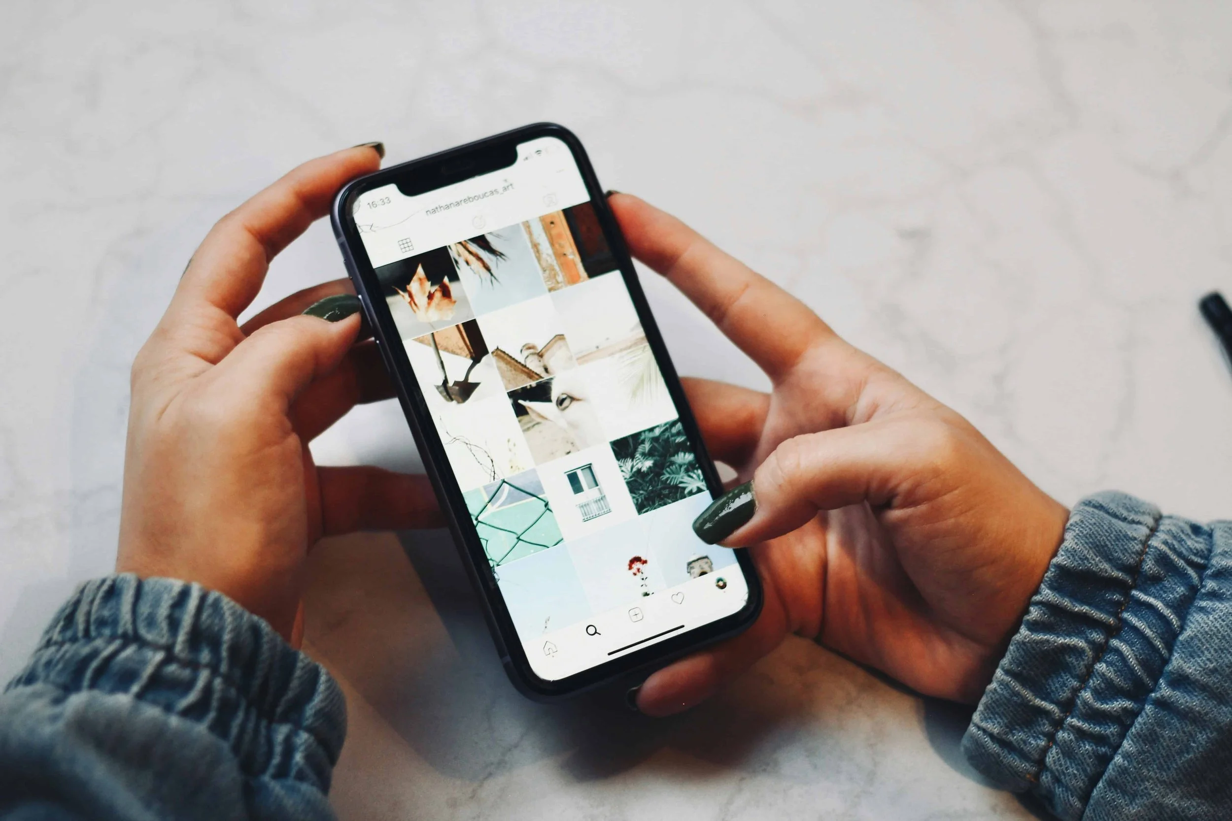 Person holding a smartphone with a gallery of images on the screen, sitting at a light-colored marble table.