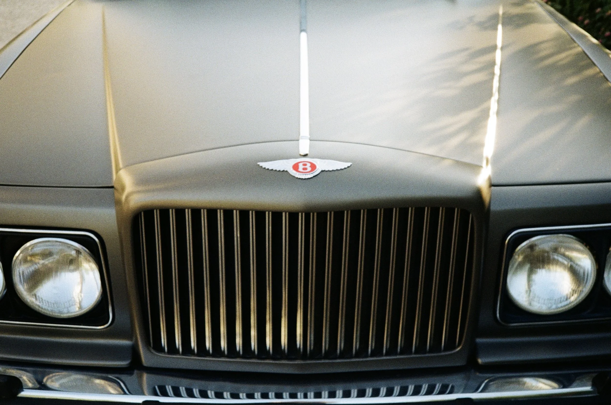 Close-up of the front grill and hood of a vintage beige Bentley car, featuring the Bentley emblem on the hood.