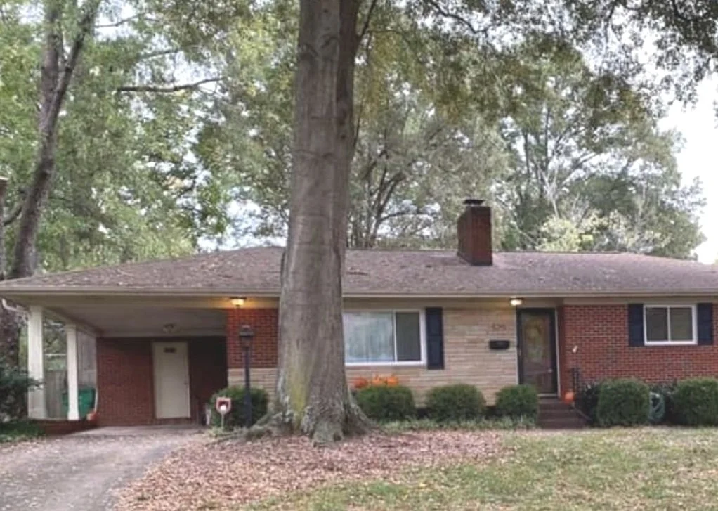 beautiful brick ranch style home with large tree in front