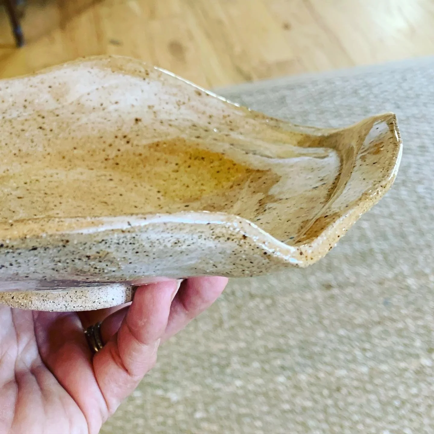 Hand holding a shallow, wavy-edged ceramic bowl with a textured, speckled surface.