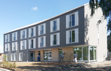 Dreistöckiges modernes Gebäude mit großen Fenstern, Männer bei Bauarbeiten vor dem Gebäude.