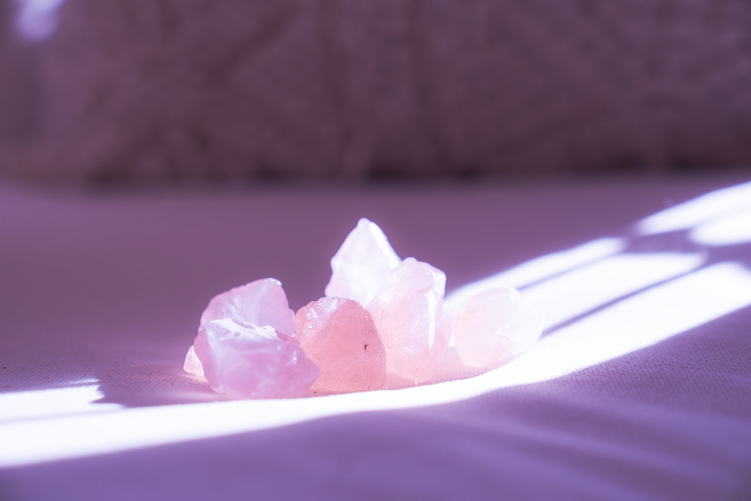 Pink Himalayan salt crystals on a purple surface with light shining and creating a bright shadow.