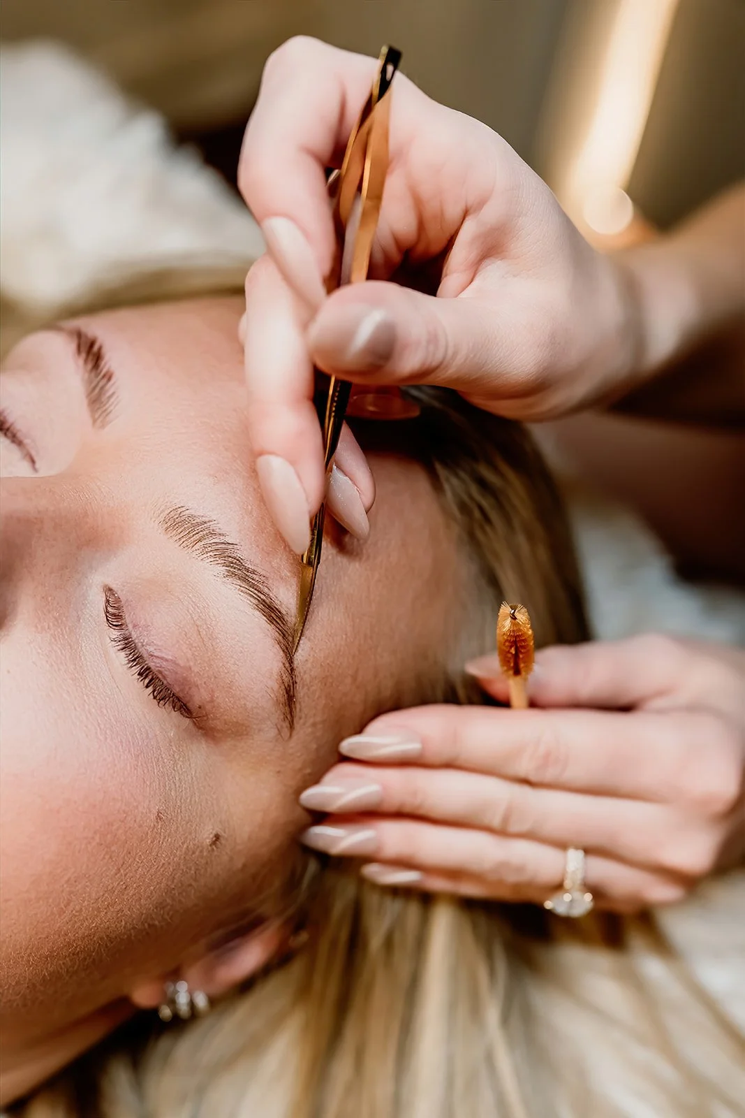 A woman getting her eyebrows microbladed by a technician using a small handheld tool.