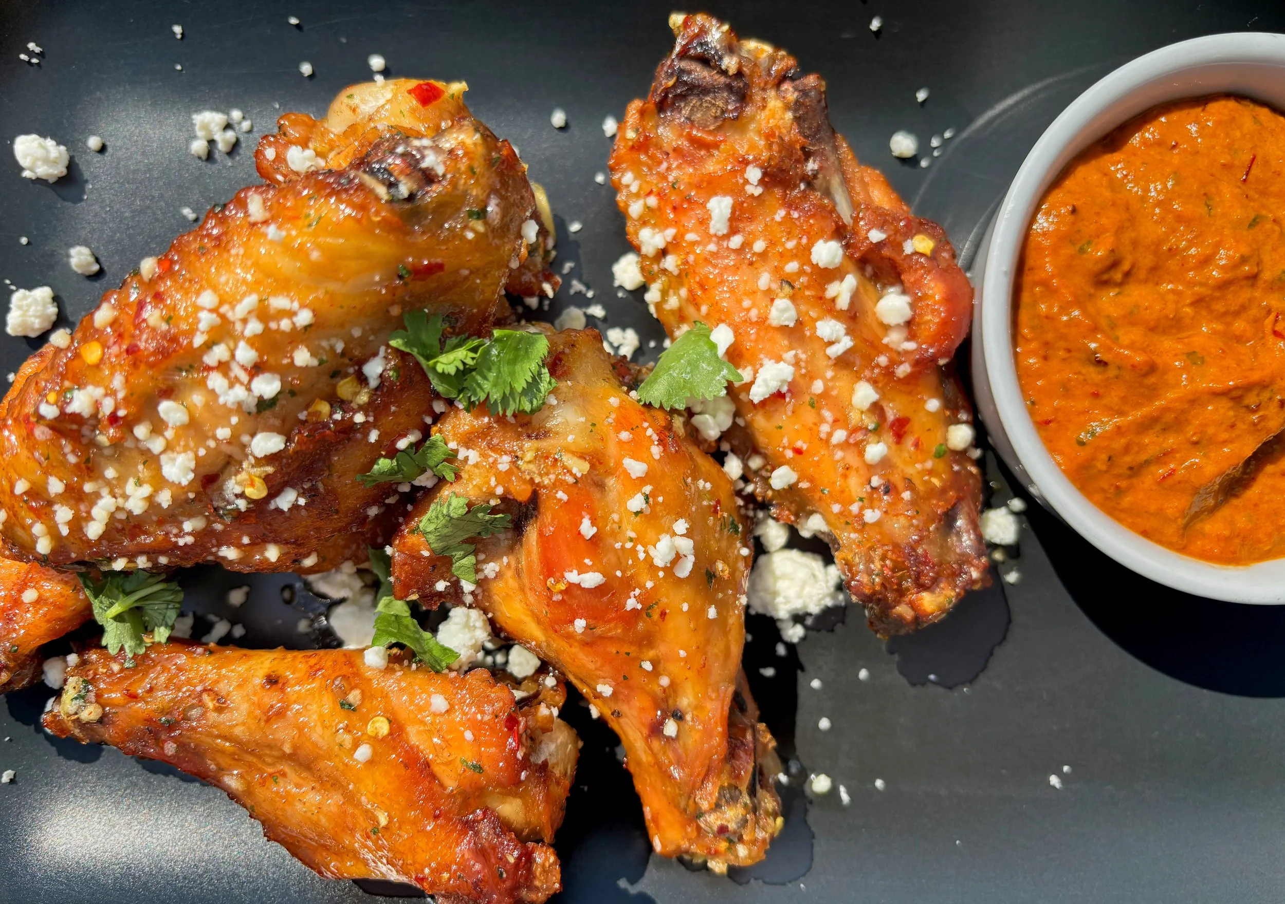 El Grito Wings: Smoky chipotle-honey wings topped with queso fresco and fresh cilantro, served with a creamy pineapple-chipotle dipping sauce.