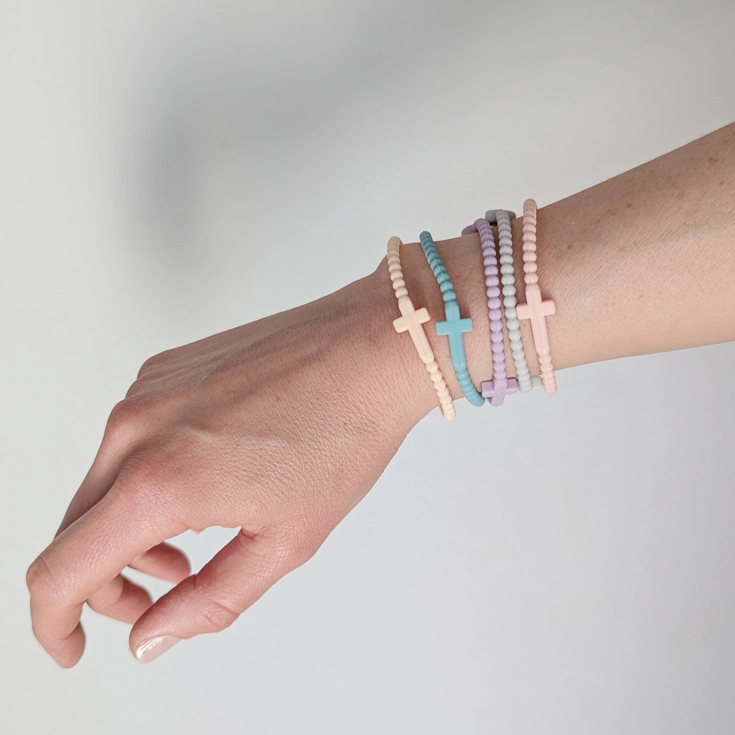 Faith silicone cross bracelets multicolor set of 5 shown in pastel stacked on a woman's wrist. Set curated by Grace Notes Ltd.