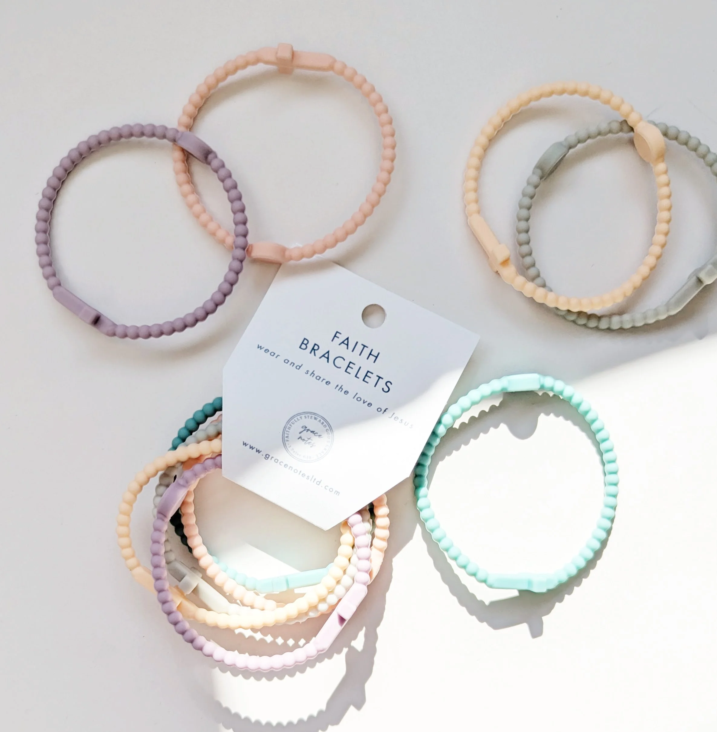 Faith silicone cross bracelets multicolor set of 5 shown in pastel in both its packaging and the bracelets loose on a table. Set curated by Grace Notes Ltd.