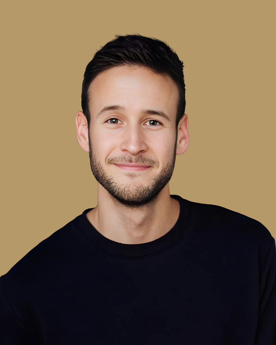 A young man with dark hair, light skin, and a beard, smiling, wearing a black shirt, against a plain beige background.