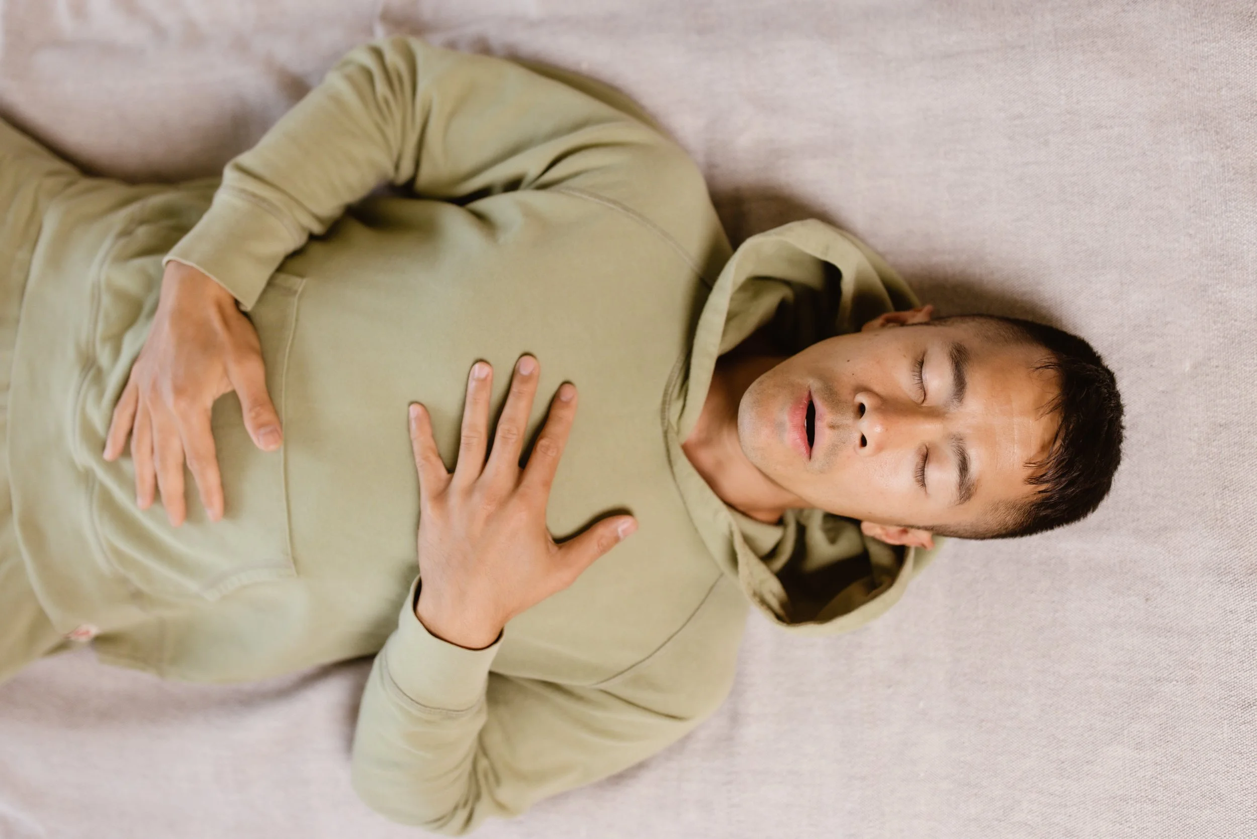 Person in a green hoodie laying down with eyes closed, hands on chest.
