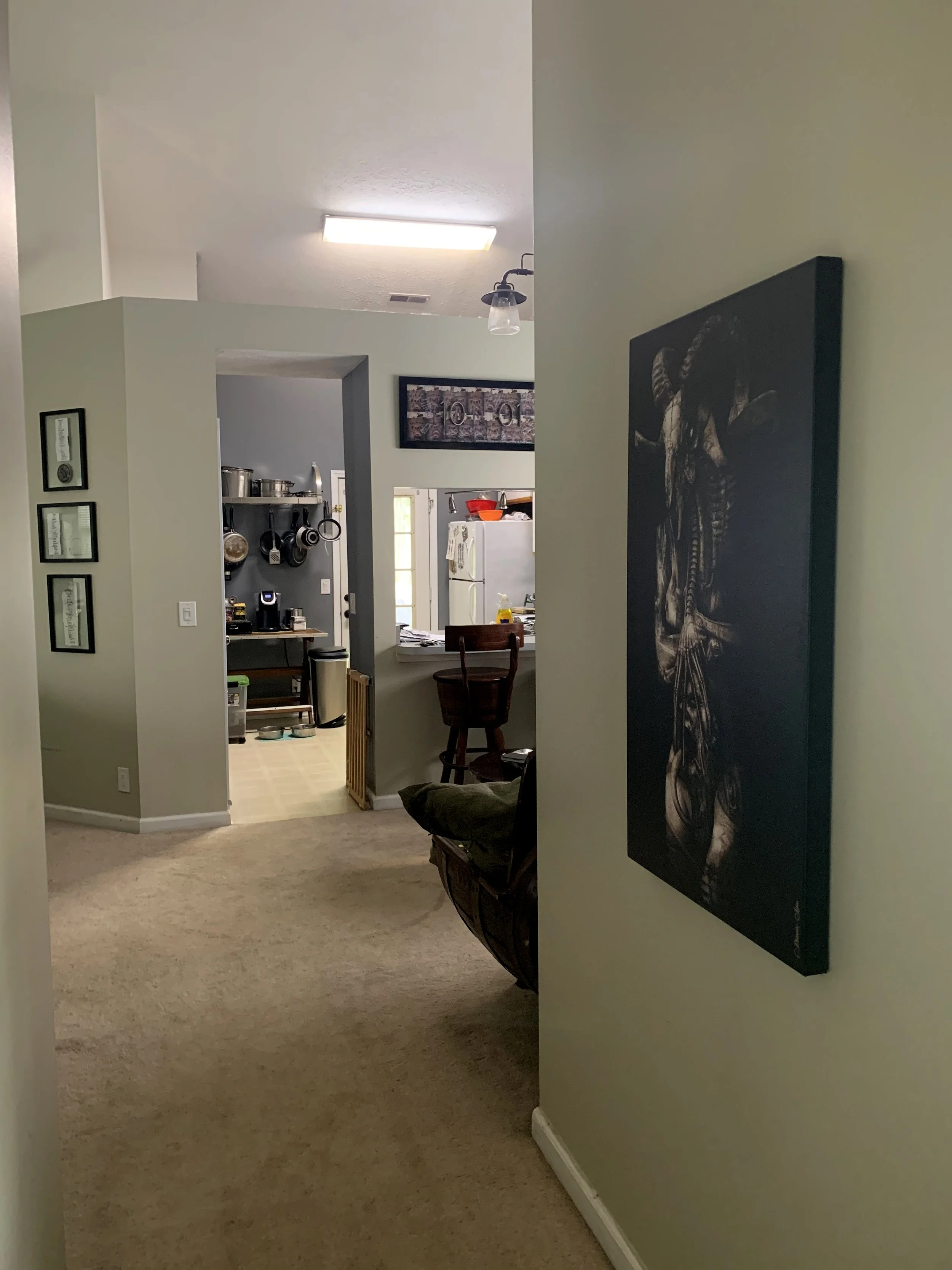 View of a hallway leading into a kitchen with a bar counter, chairs, and hanging pots and pans on the wall.