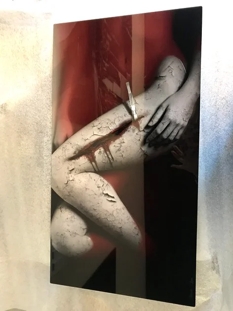 Mixed media artwork depicting a humanoid figure with cracked and peeling skin, with a face profile, painted in black, white, and red tones.