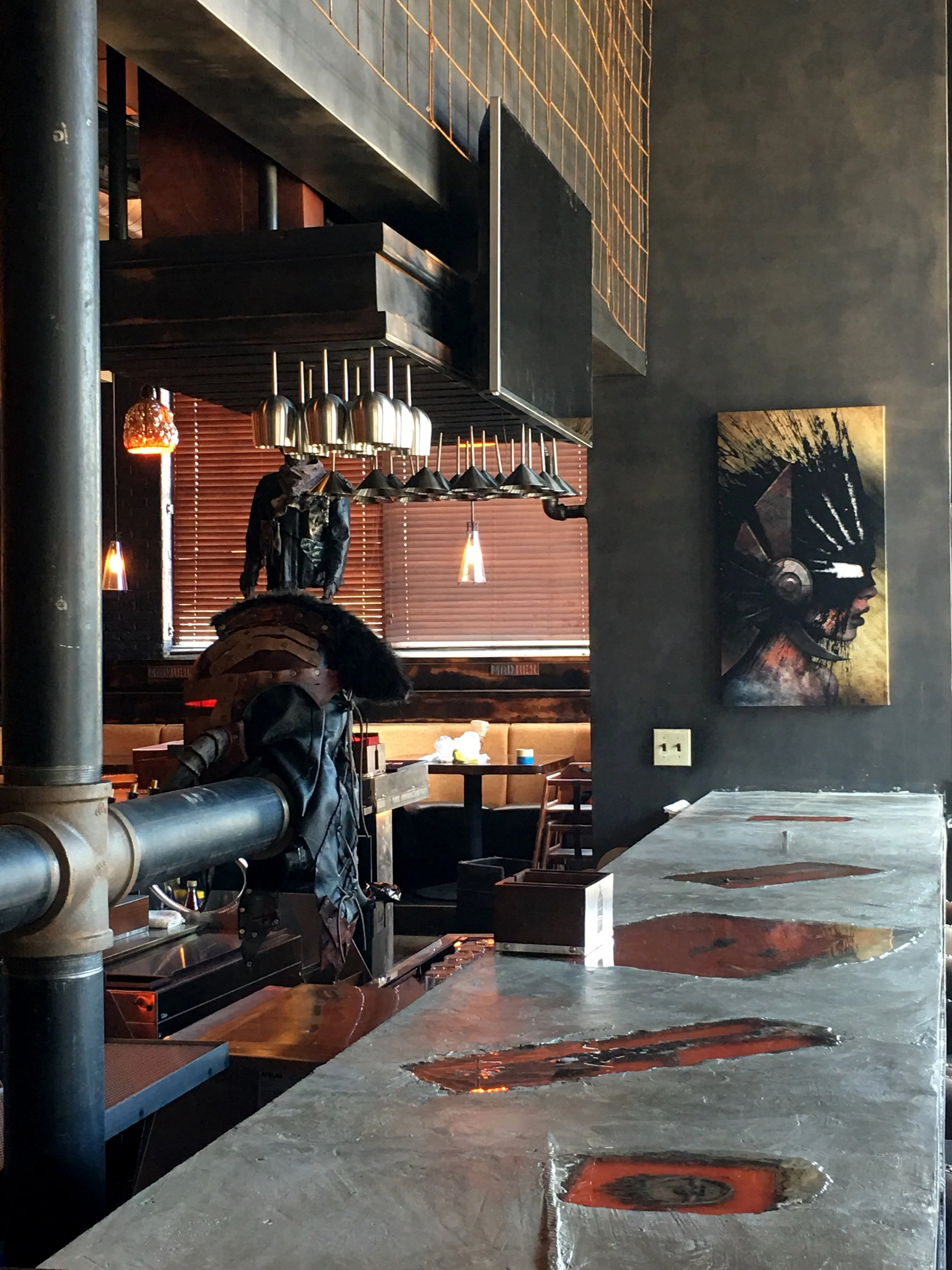 Interior of a restaurant or bar with a counter, modern hanging lights, artwork on black wall, and graffiti-style portrait art on the wall.
