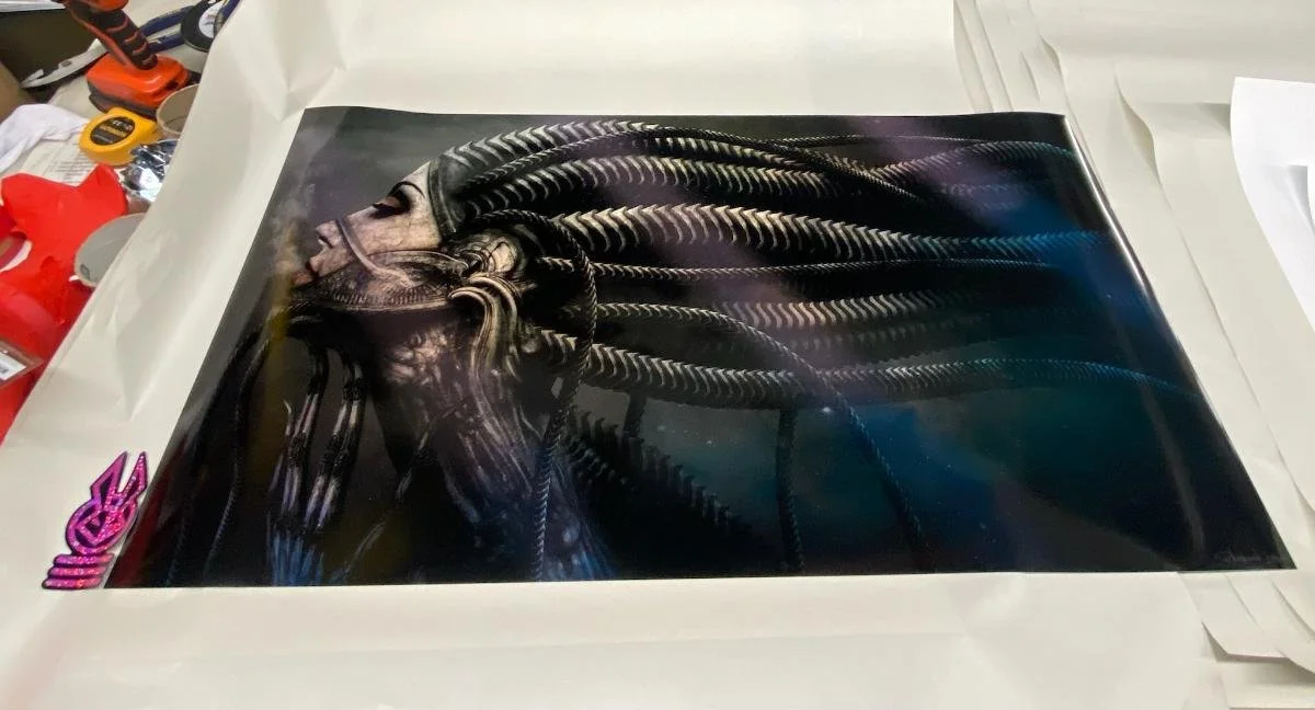 A printed poster of a woman with long, intricate hair made of metallic, braided strands, lying on a white surface with various tools and items around it.
