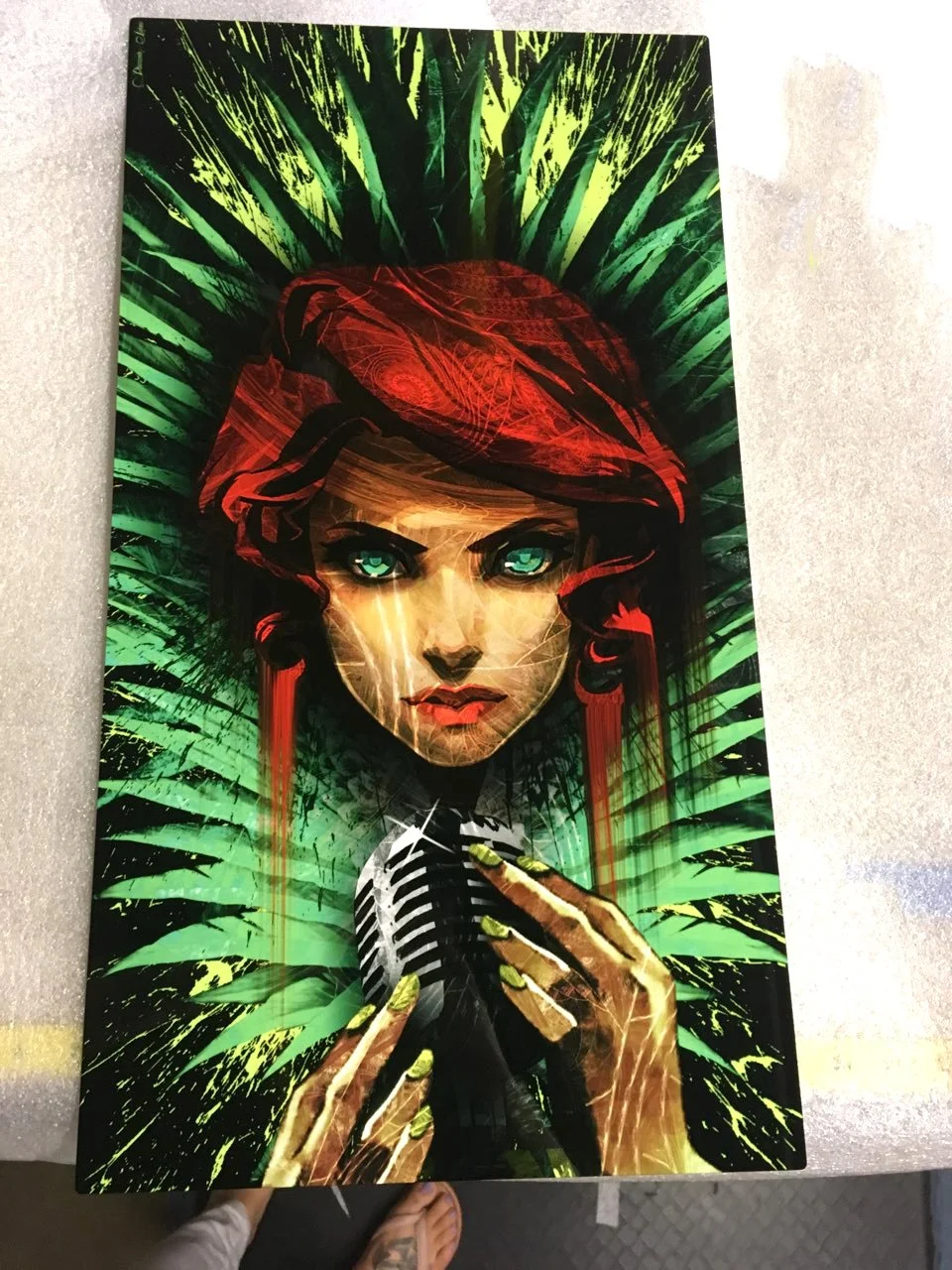 A vibrant poster illustration of a woman with teal eyes, red hair, and green nails, holding a black and white striped microphone, surrounded by green palm leaves with a dark background.