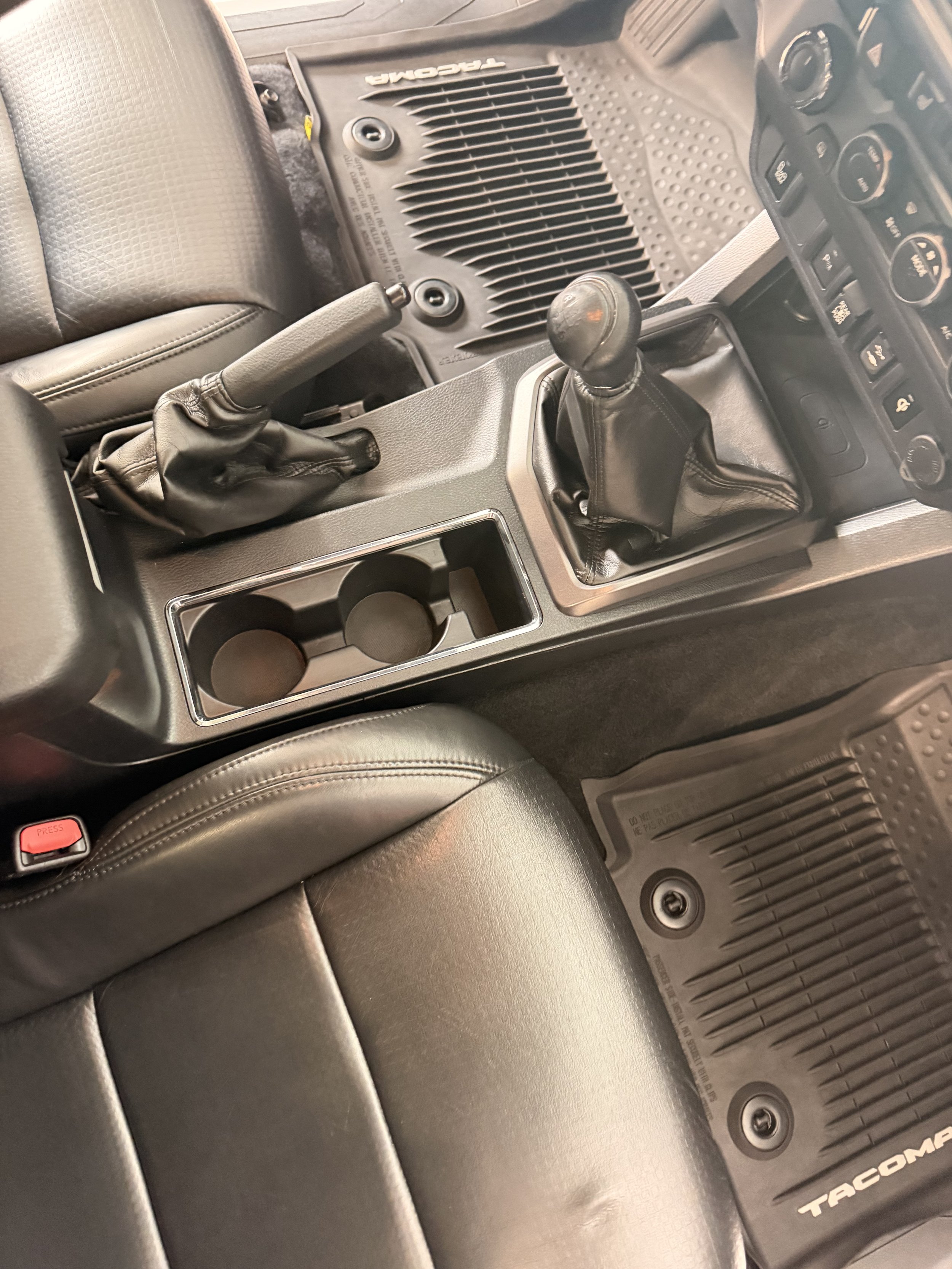Interior of a vehicle showing the gearshift, handbrake, rubber mats, cup holders, and dashboard controls.