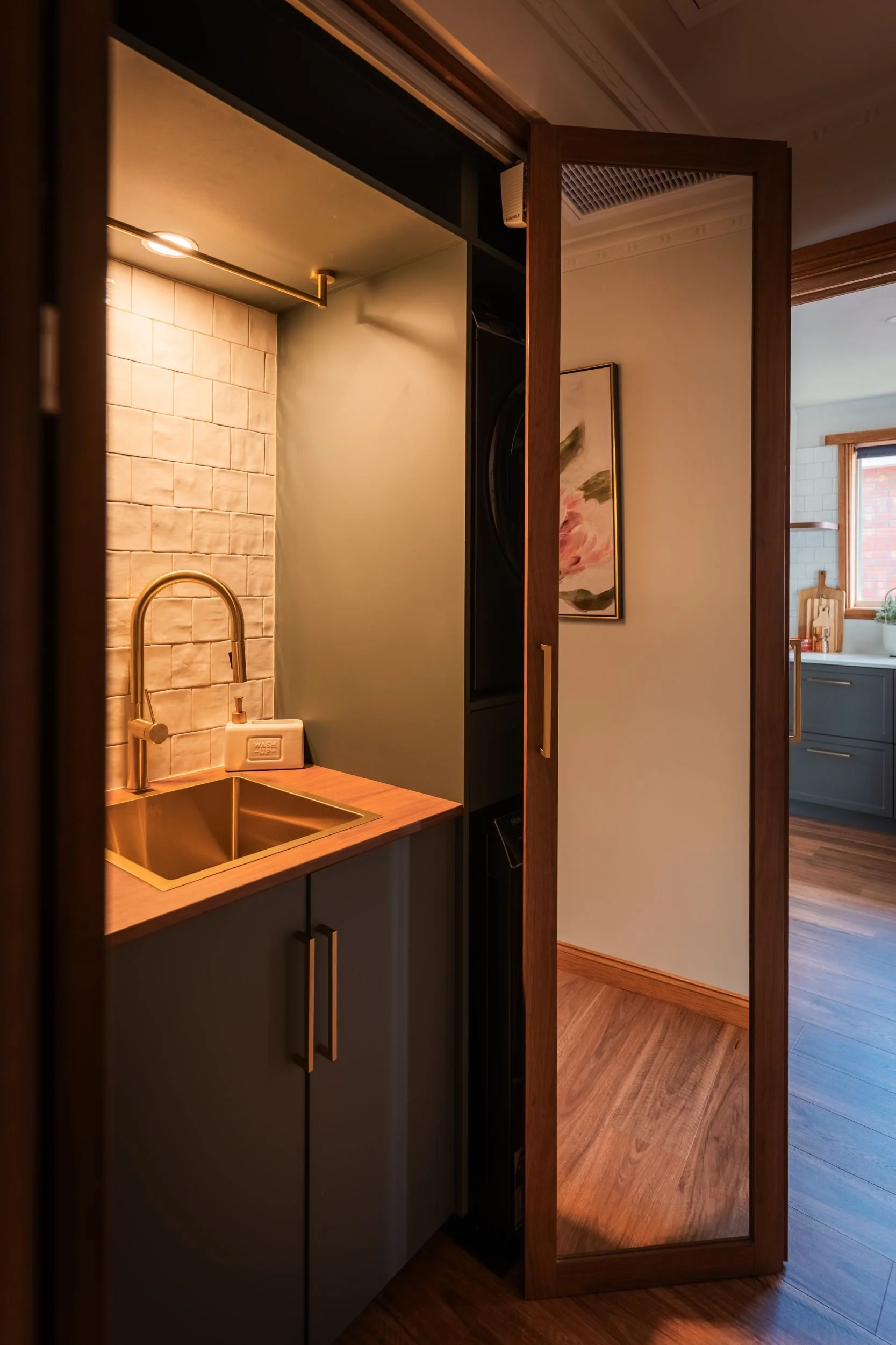 Lit laundry nook with brass sink behind a concealed door