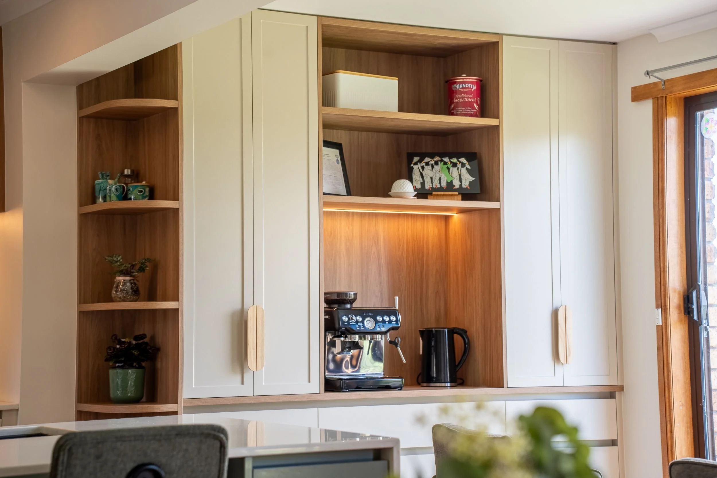 Tall white pantry joinery with a timber-lined coffee nook and curved open shelves