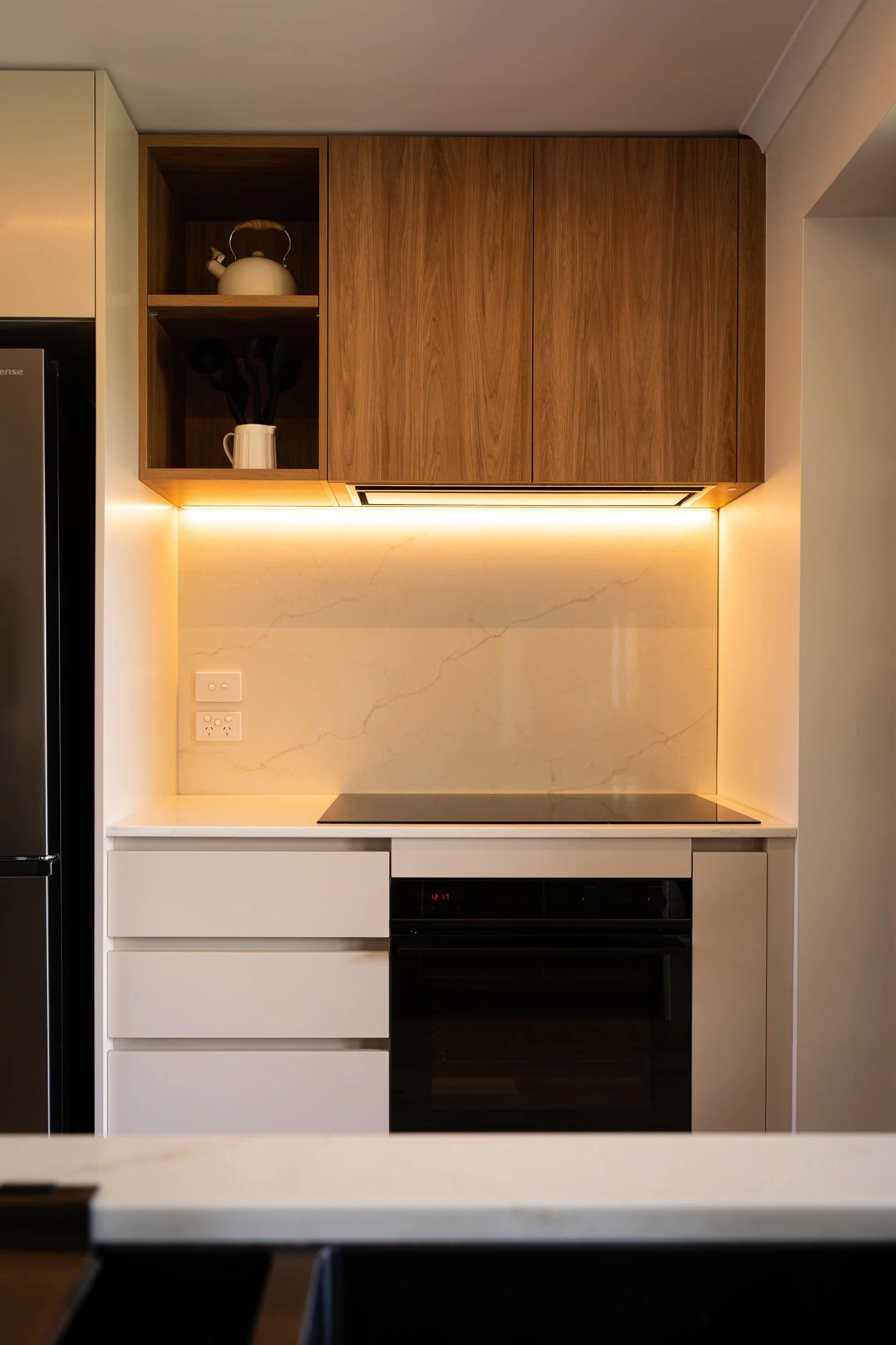Oven and cooktop under timber overhead cabinets with LED strip lighting