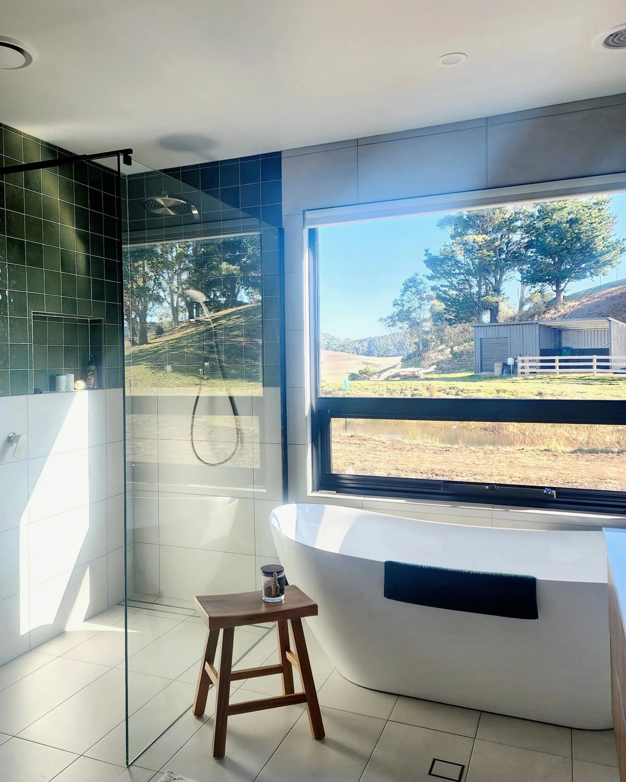 Freestanding bath and green-tiled shower framed by garden views — softly layered bathroom interiors designed by Tahleah Hoyle.