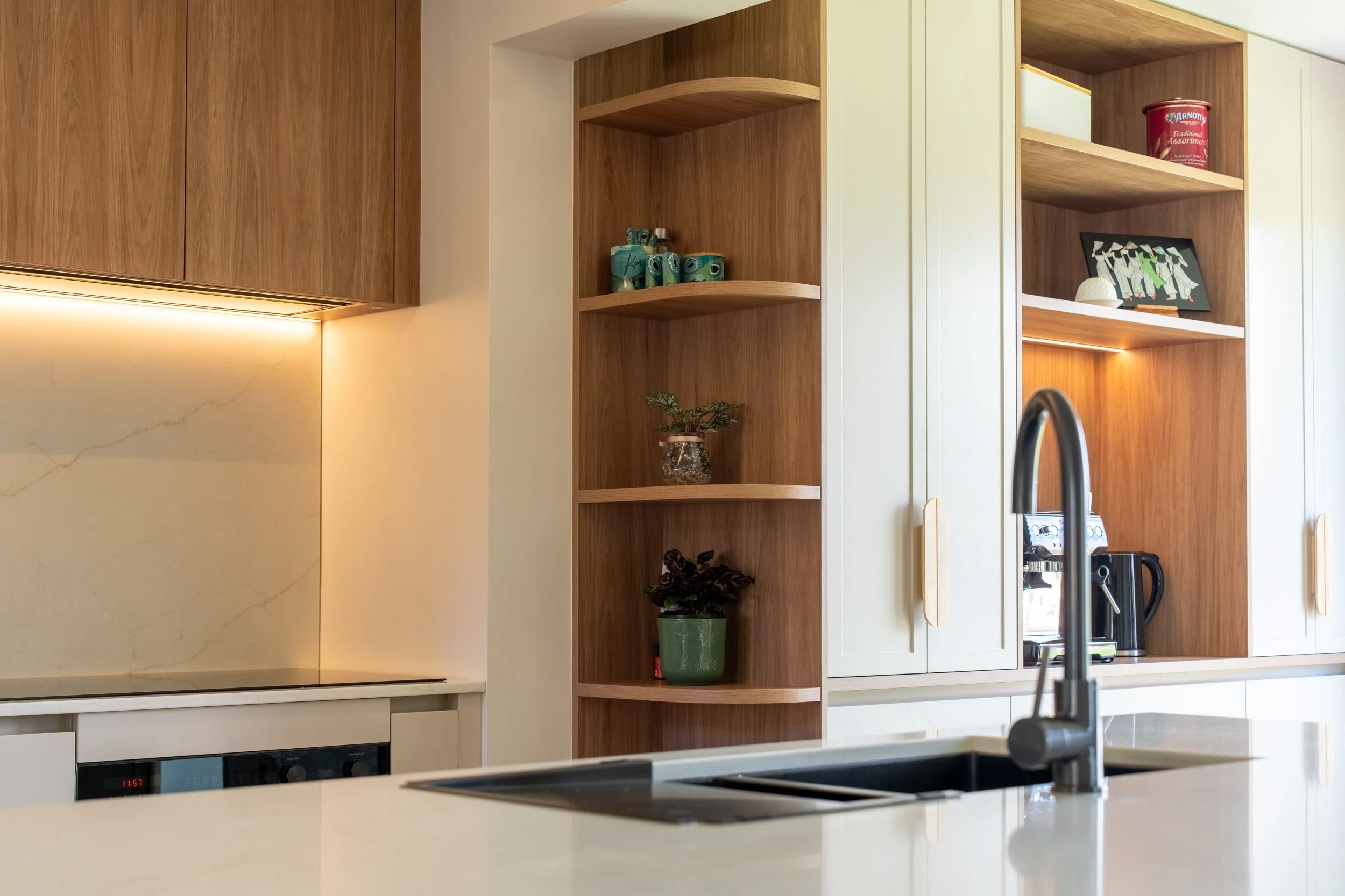 Gunmetal sink and tap with curved timber shelving and under-cabinet lighting