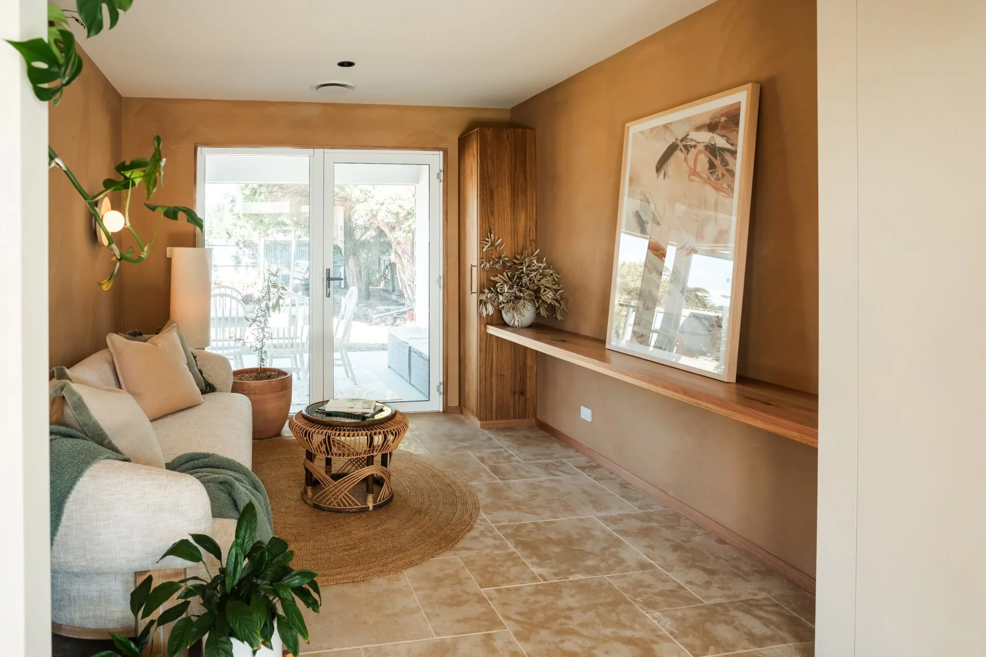 Conservatory sitting room at Raeburn with earthy limewash walls, timber shelving and soft furnishings.