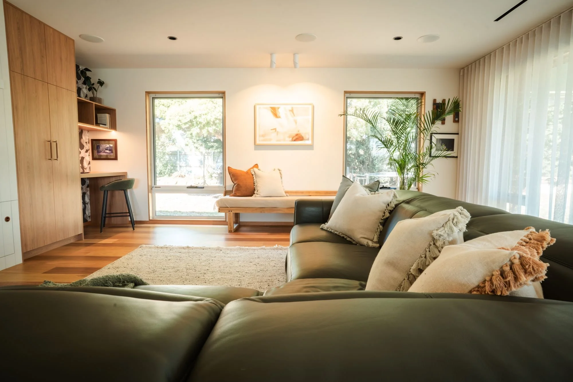 Living room at Raeburn featuring custom wall joinery, timber floors and large windows.