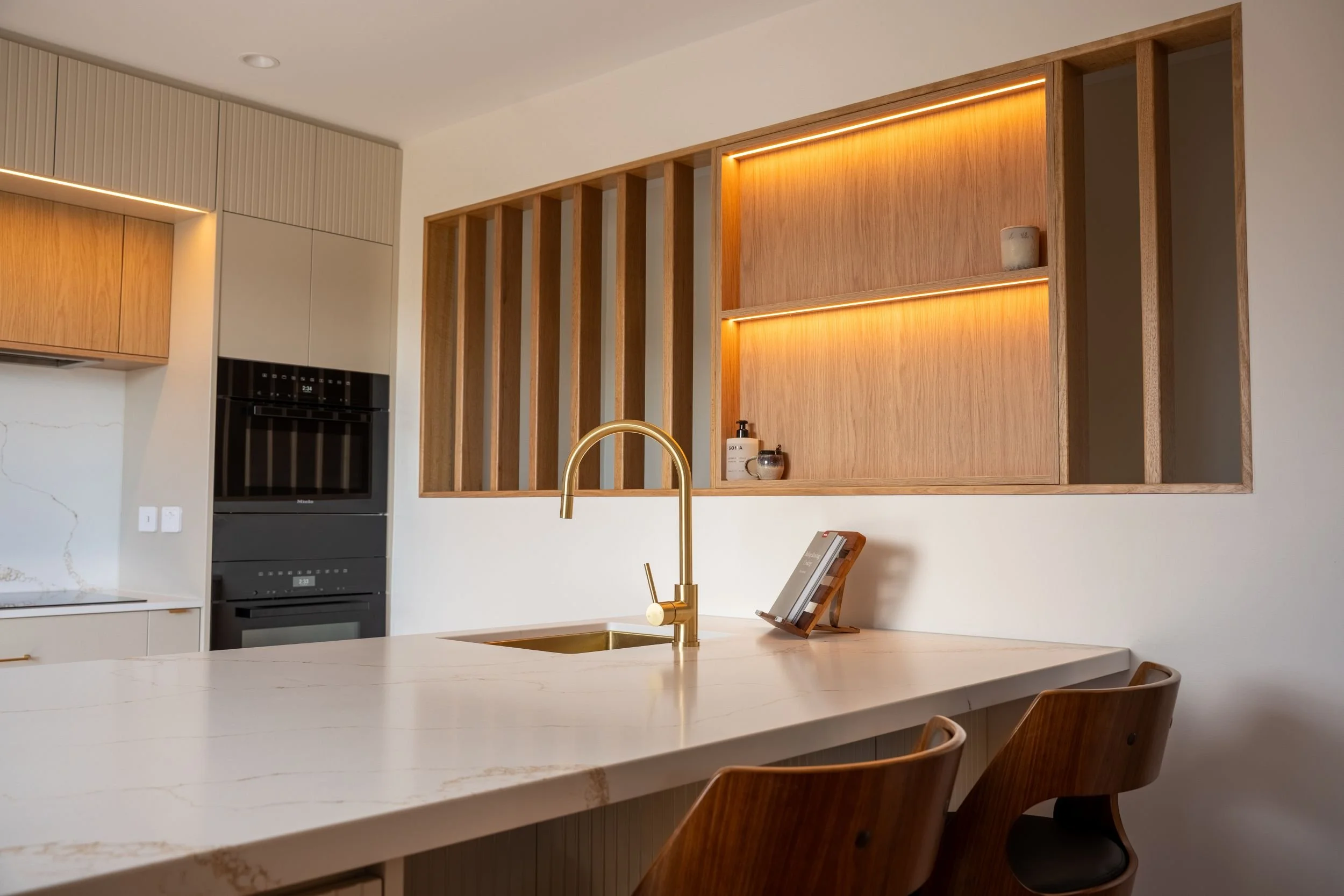 Kitchen sink with brass gooseneck tap and timber batten screen with LED lighting