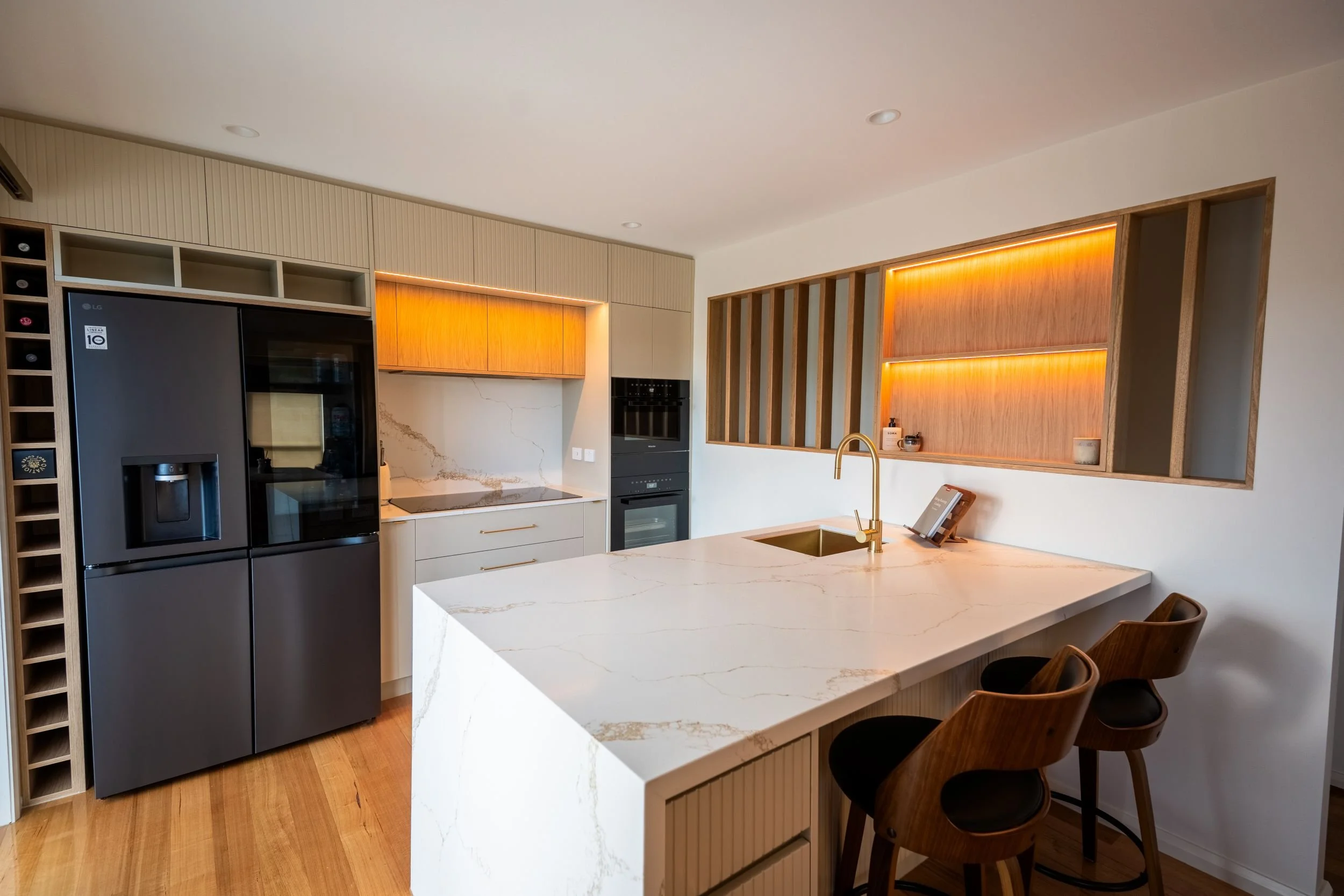 Waterfall stone island with brass tap and integrated wine rack beside the fridge