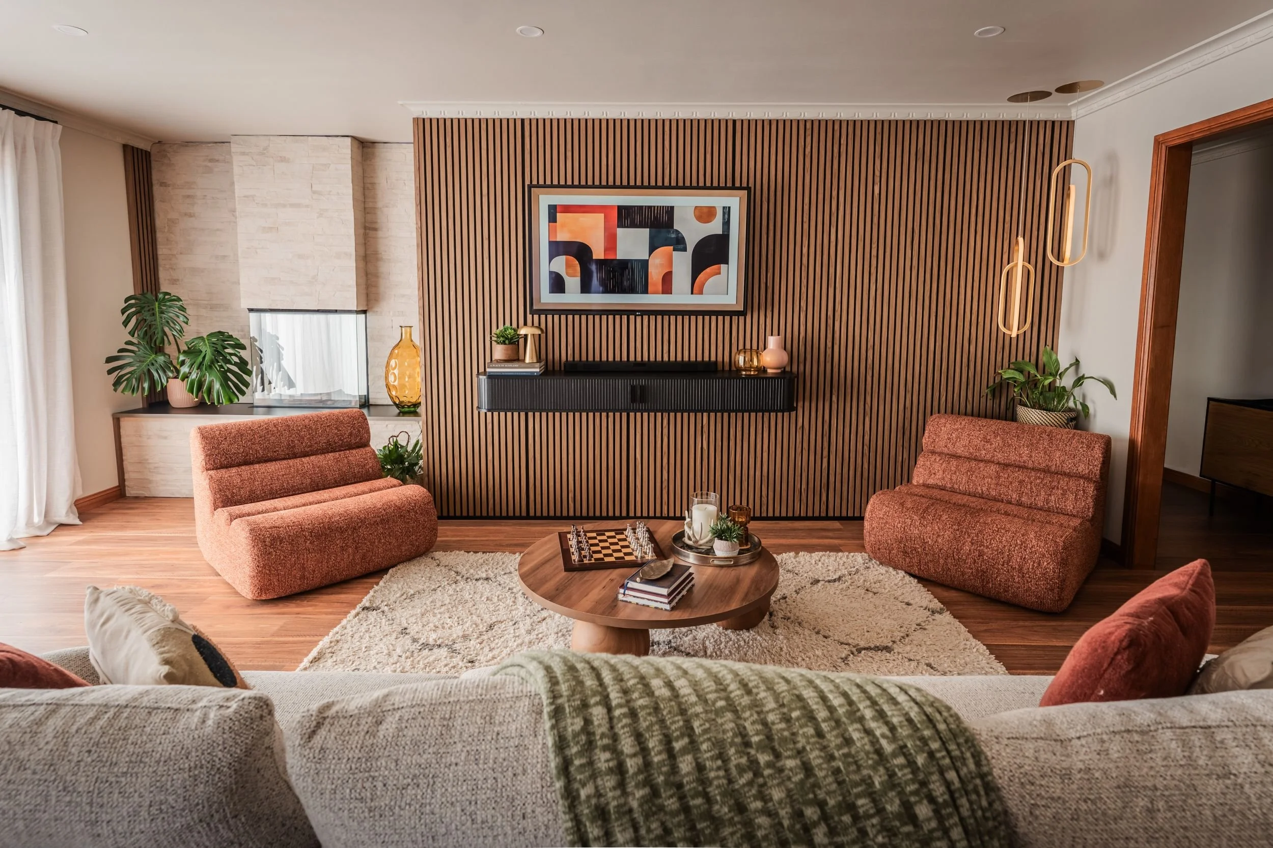 Living room with walnut batten feature wall, terracotta armchairs and abstract artwork