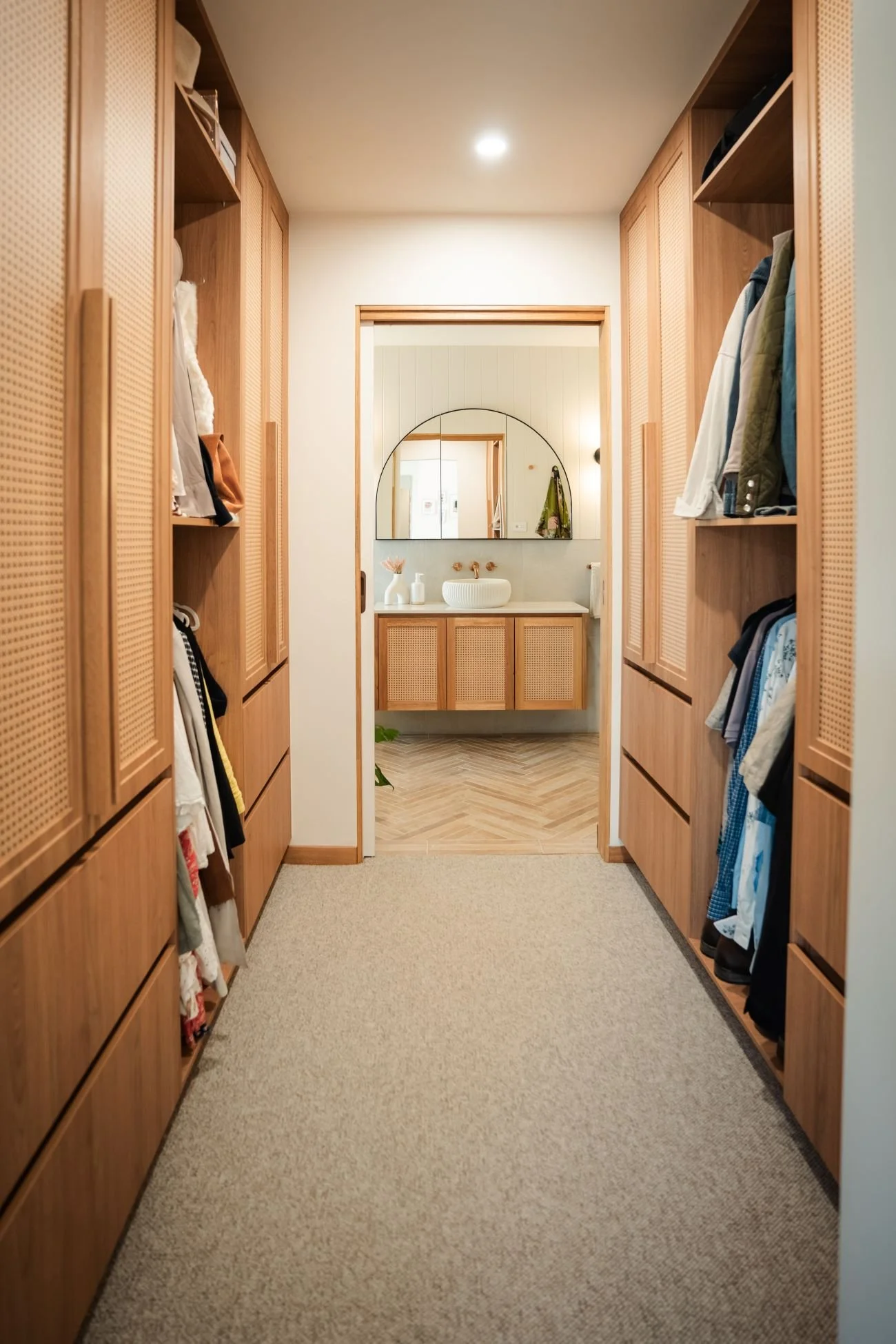 Walk-in robe leading to ensuite bathroom at Raeburn with timber cabinetry and herringbone tile flooring.