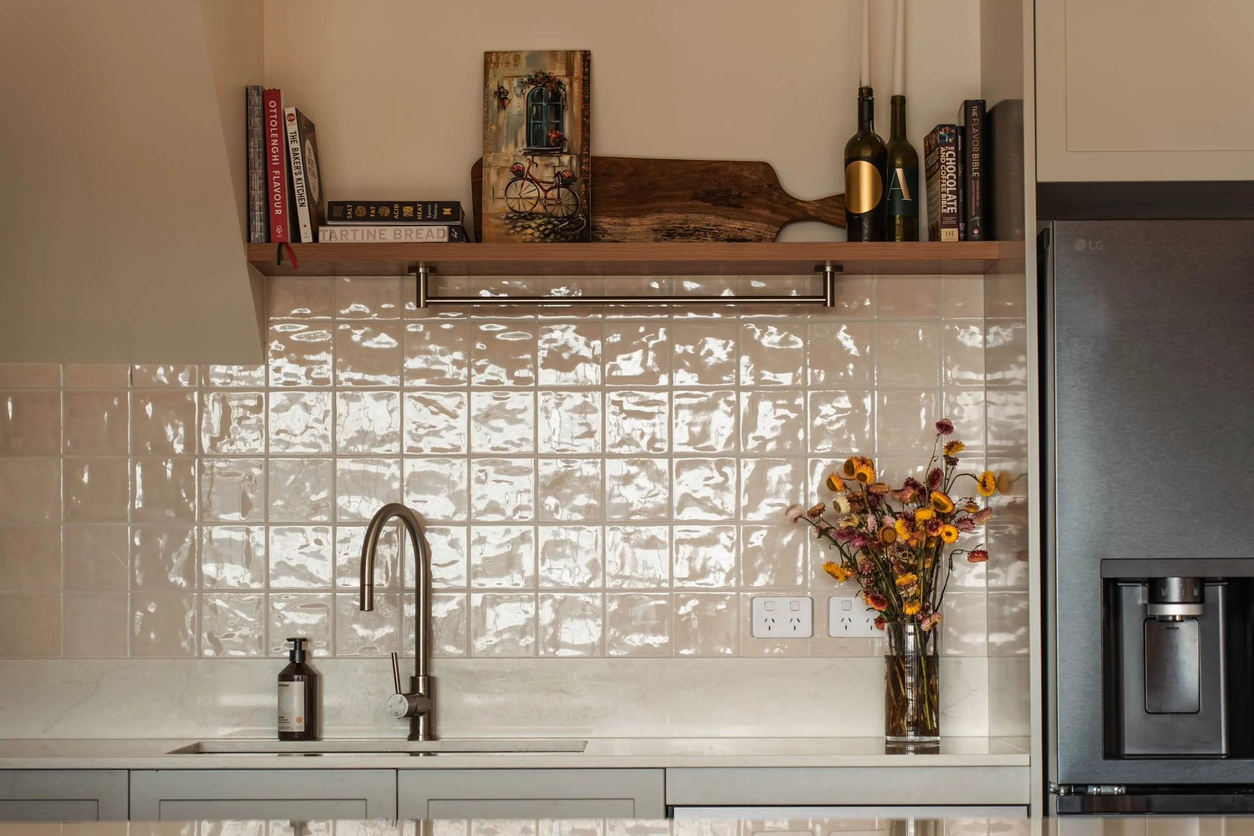 Glossy handmade-look tiled splashback with brushed chrome tap and timber shelf